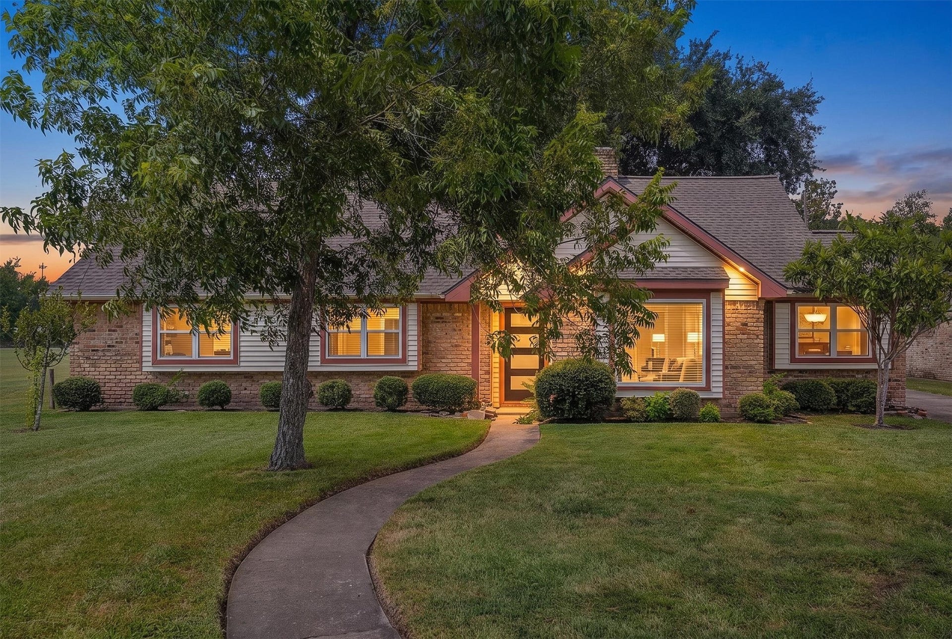 2503 Moss Hill Drive, Houston, TX 77080 Brick home with warm, inviting lighting, surrounded by lush greenery and a winding walkway, perfect for cozy evenings.