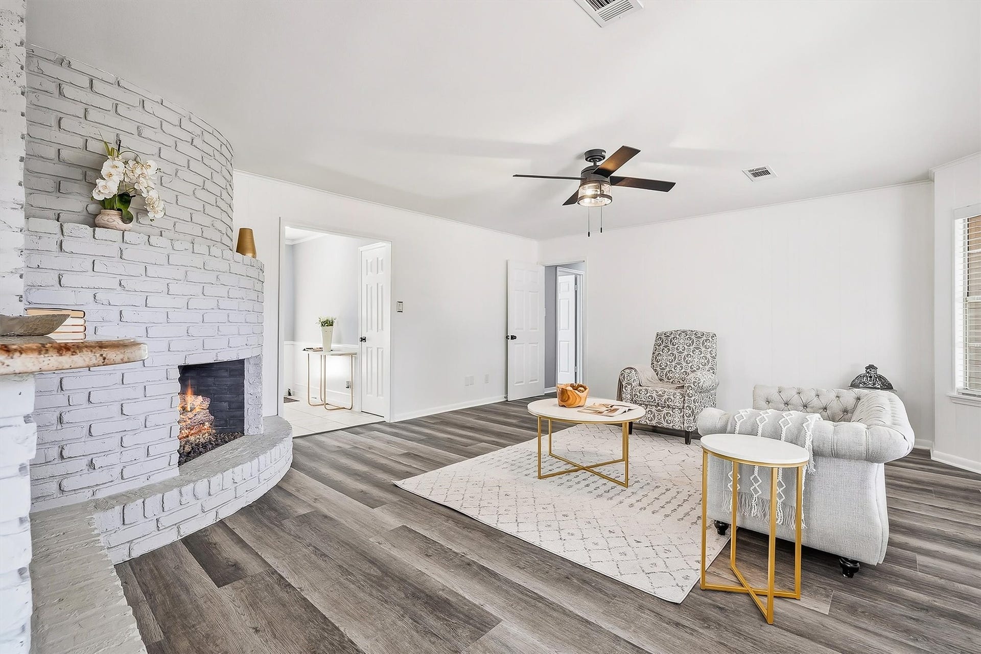 2503 Moss Hill Drive, Houston, TX 77080 Living room featuring a stylish curved brick fireplace, elegant vinyl plank flooring, and a modern ceiling fan, perfect for relaxation and gatherings.