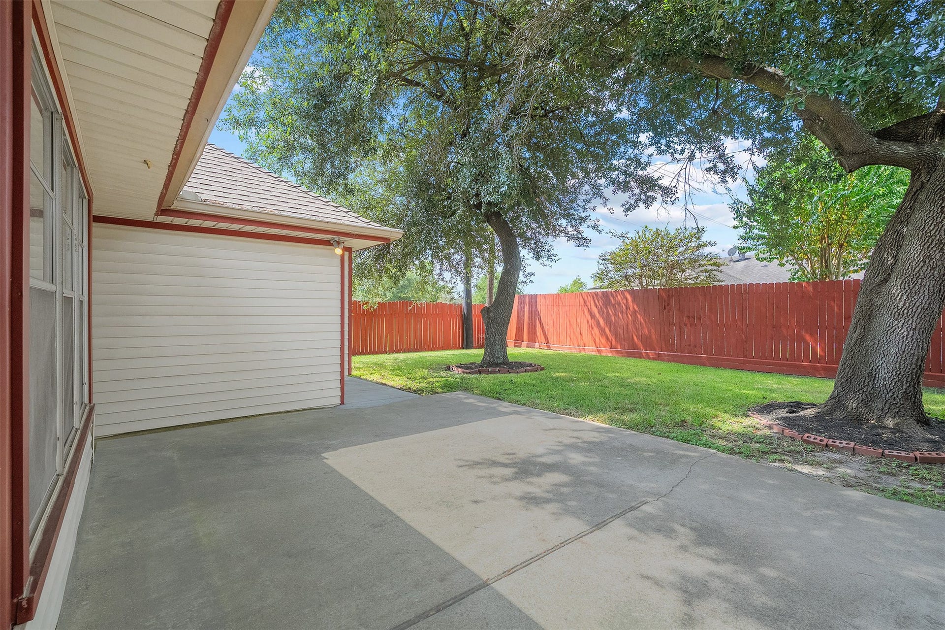 2503 Moss Hill Drive, Houston, TX 77080 Charming backyard patio with a spacious concrete area, perfect for outdoor seating, shaded by mature trees, and bordered by a warm wooden fence for privacy.