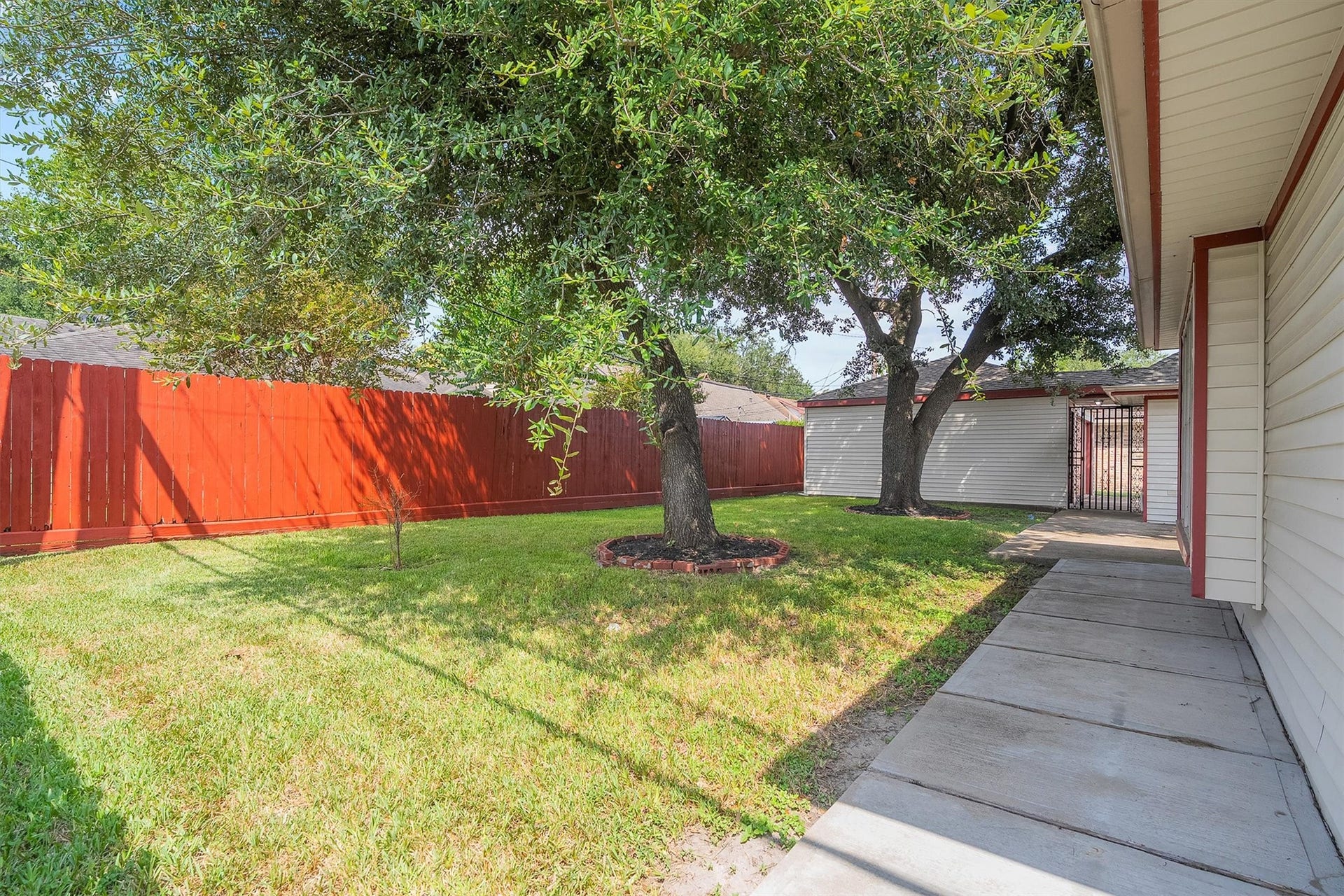 2503 Moss Hill Drive, Houston, TX 77080 Charming backyard offers lush greenery and mature trees providing ample shade, complemented by a striking red fence for privacy and a cozy walkway.