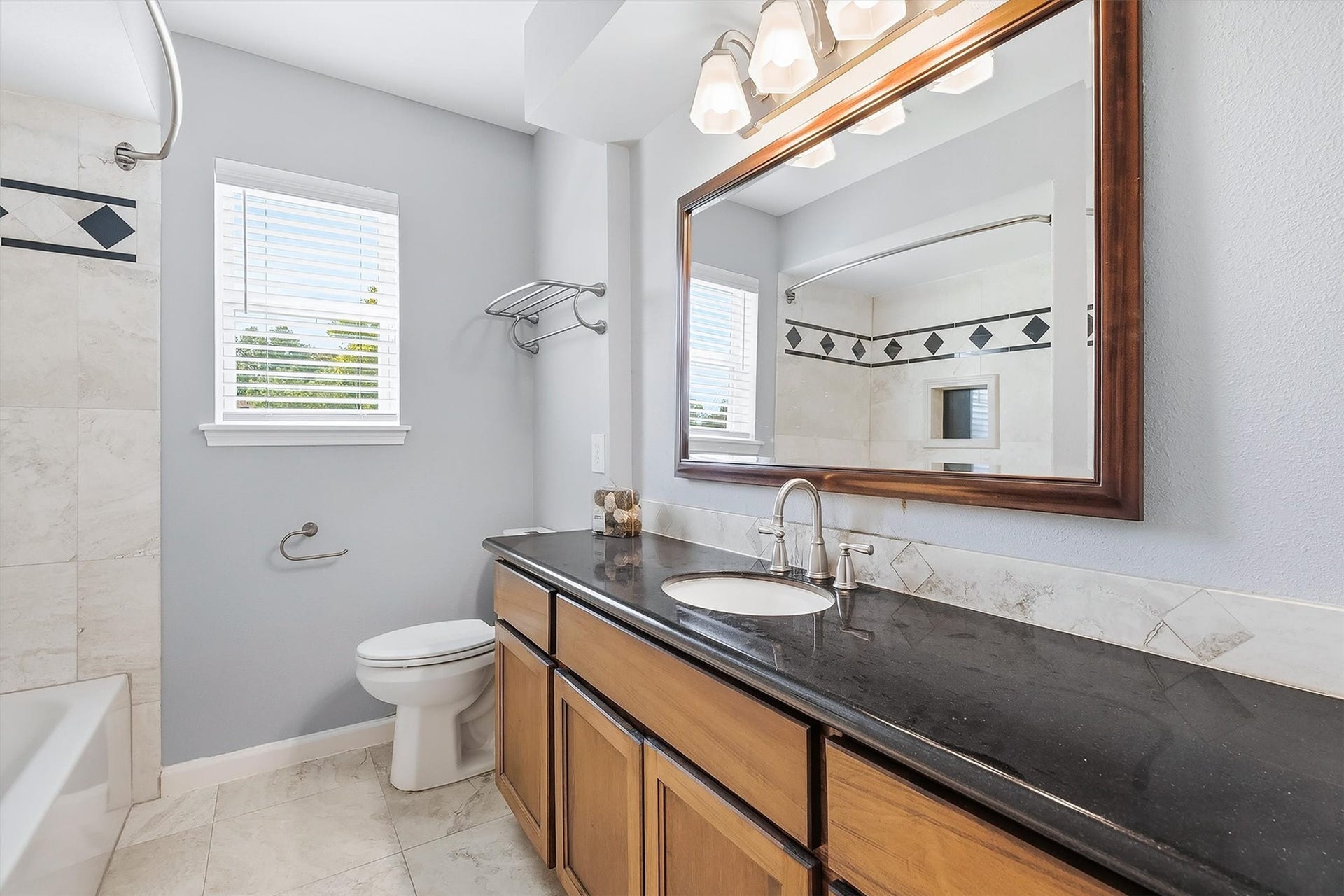 2503 Moss Hill Drive, Houston, TX 77080 Elegant Guest bathroom with a sleek black countertop, ample storage, and a large framed mirror. Natural light streams through the window, highlighting the stylish tile work and modern fixtures.