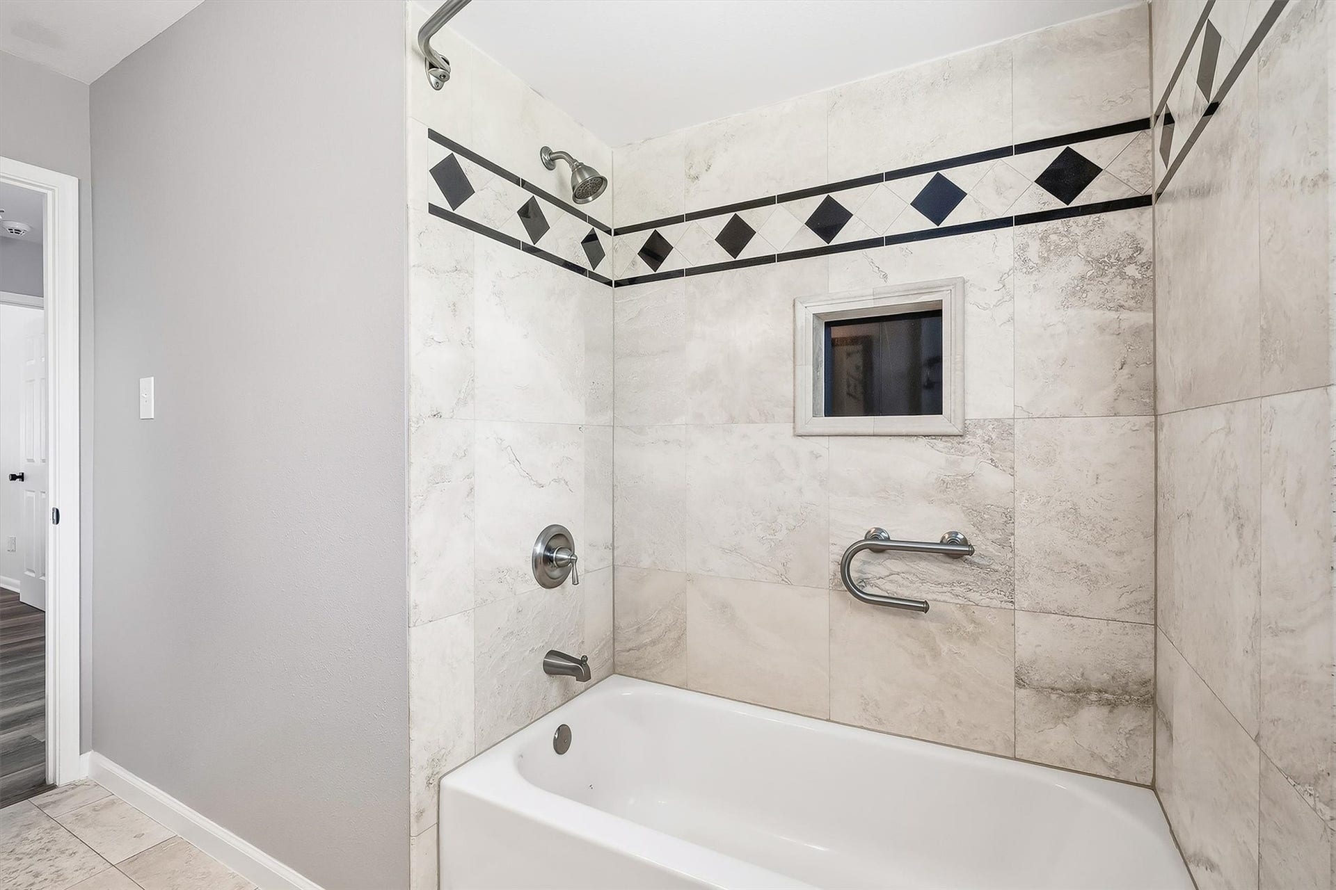 2503 Moss Hill Drive, Houston, TX 77080 Elegant guest bathroom featuring a tiled shower and tub with a stylish black and white diamond accent, complemented by a convenient built-in shelf.