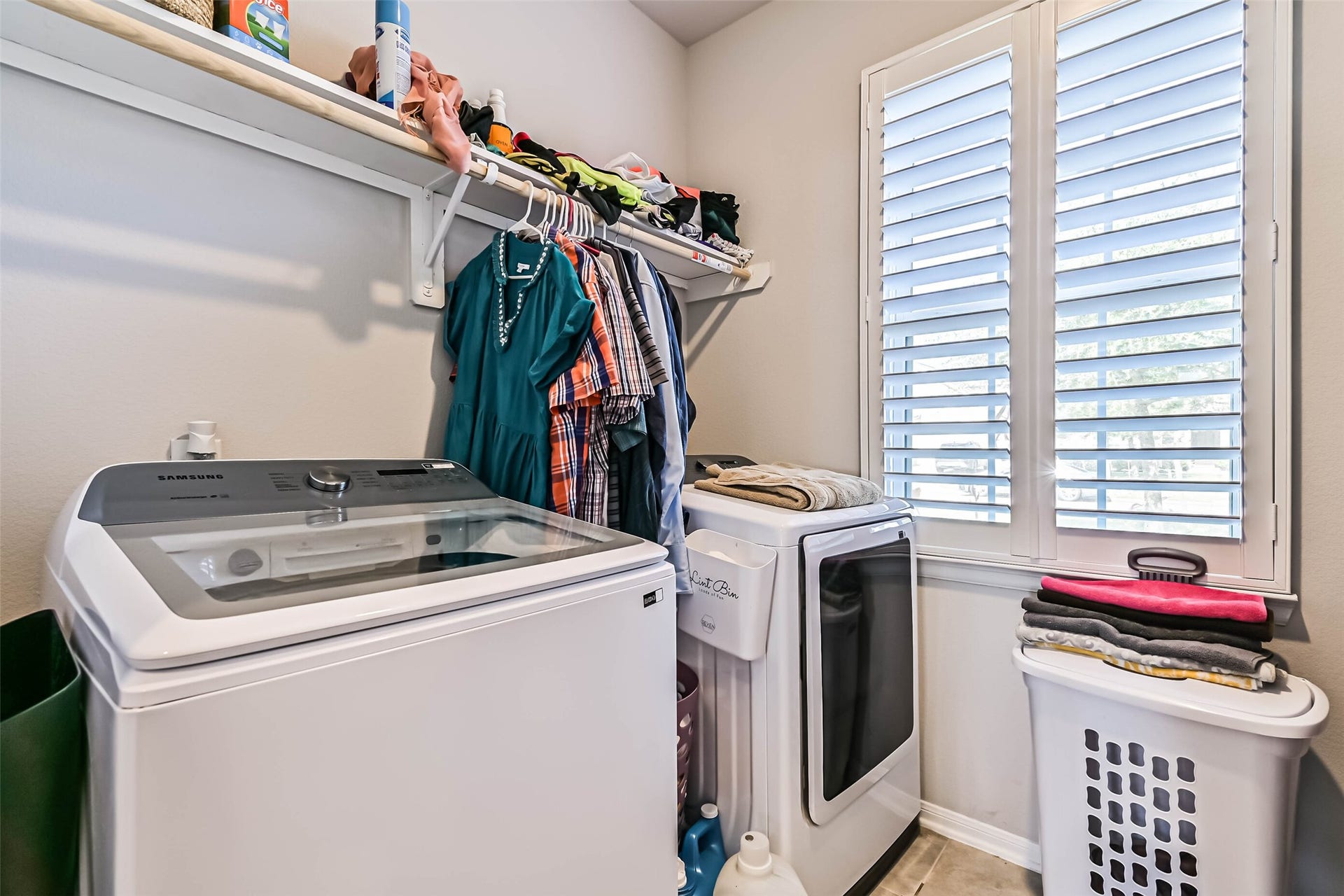 12527 Jetty Cove Drive, Texas City, TX 77568 Dedicated laundry room featuring washer and dryer space, overhead shelving, hanging storage, and a window with plantation shutters.
