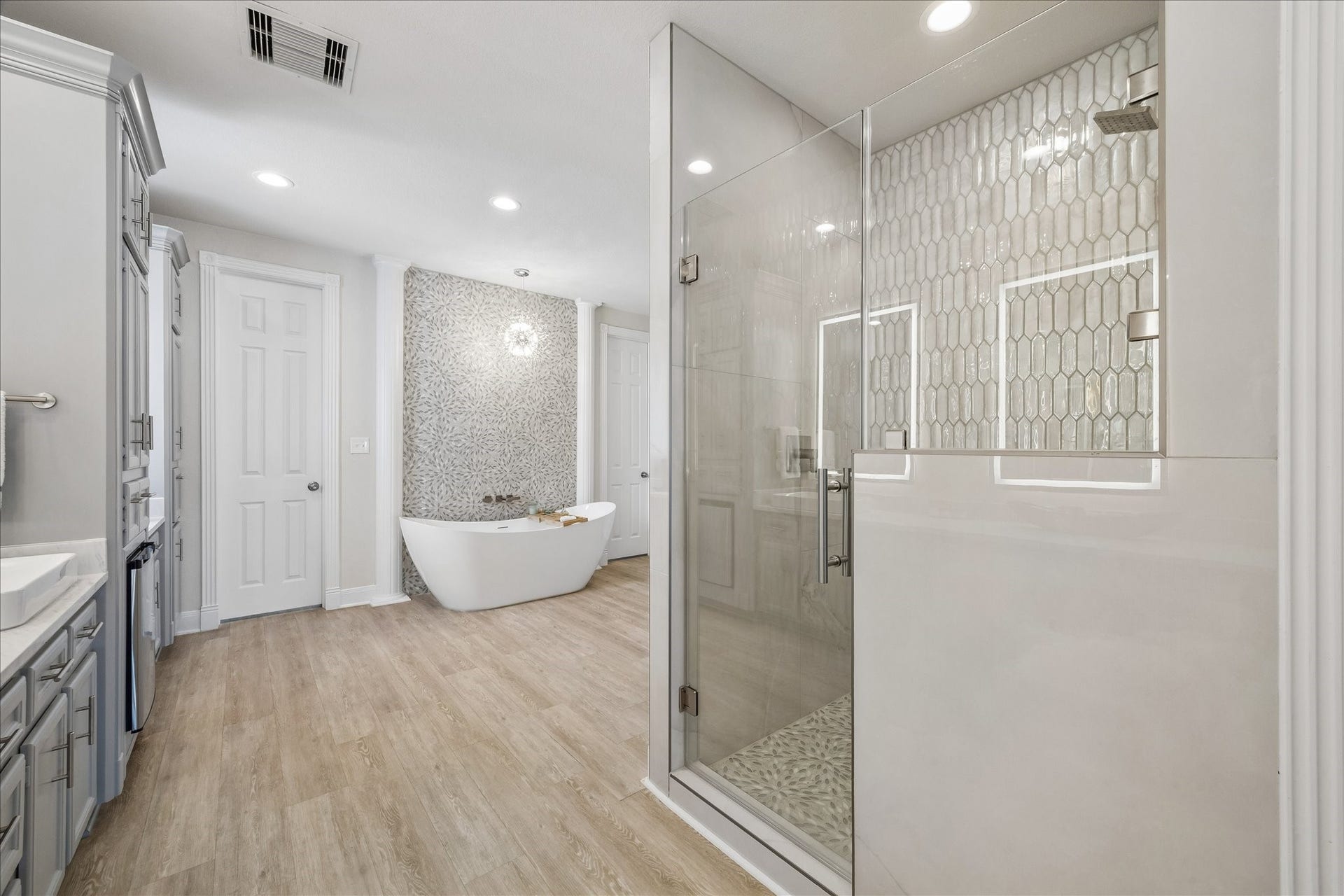 426 Sunset Circle, Tiki Island, TX 77554 Relax and unwind in the elegant soaking tub, framed by a striking tiled accent wall. The light and airy finishes create a serene retreat within the completely remodeled primary bathroom. Remodel includes: a new shower, bathtub, sinks, faucets, flooring, mirrors, towel bars, beverage refrigerator & lighting.
