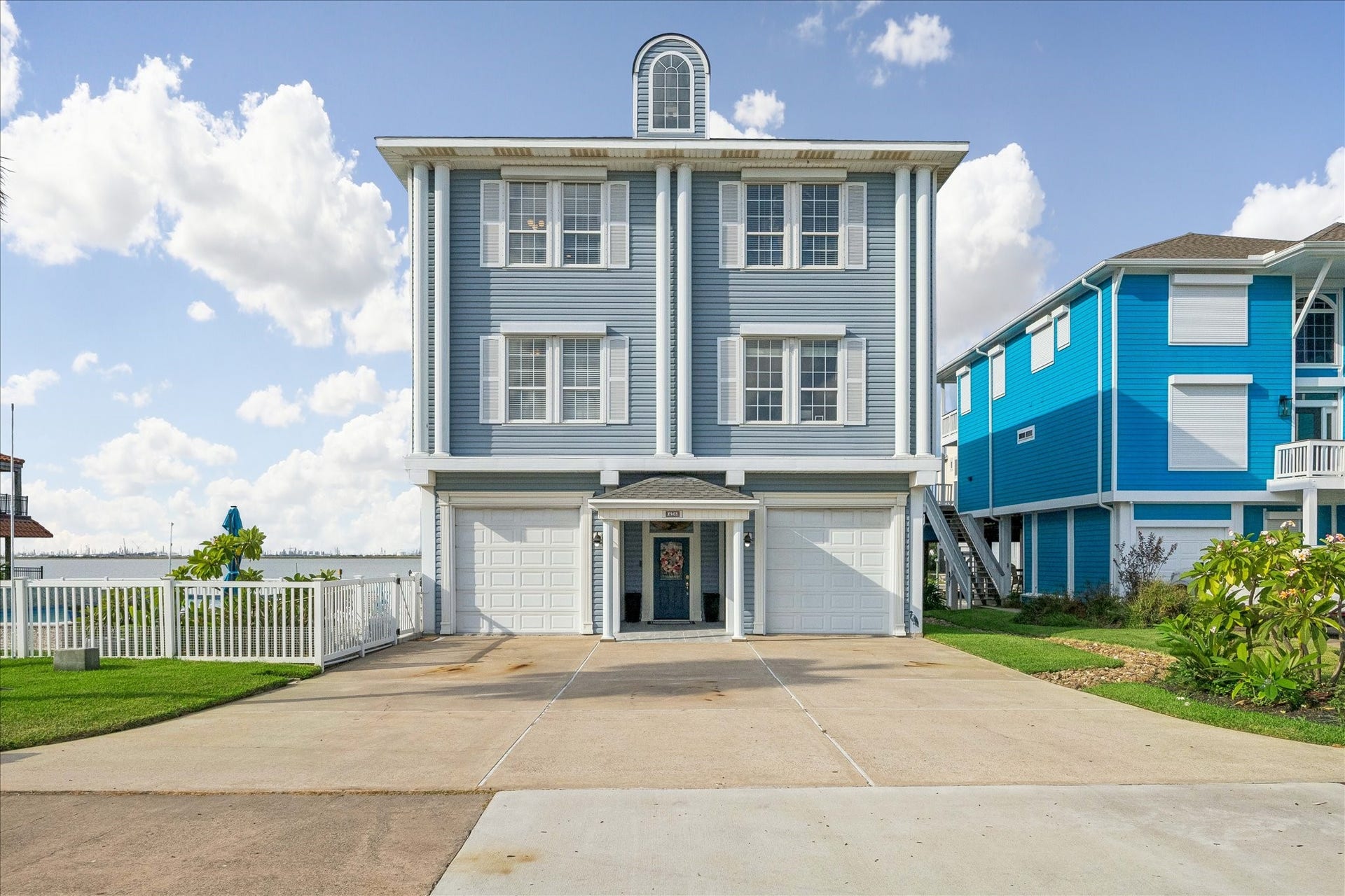 426 Sunset Circle, Tiki Island, TX 77554 Charming coastal home featuring a classic blue exterior with white trim, spacious three-story design, New tile flooring in outdoor entryway all set against a serene waterfront backdrop.