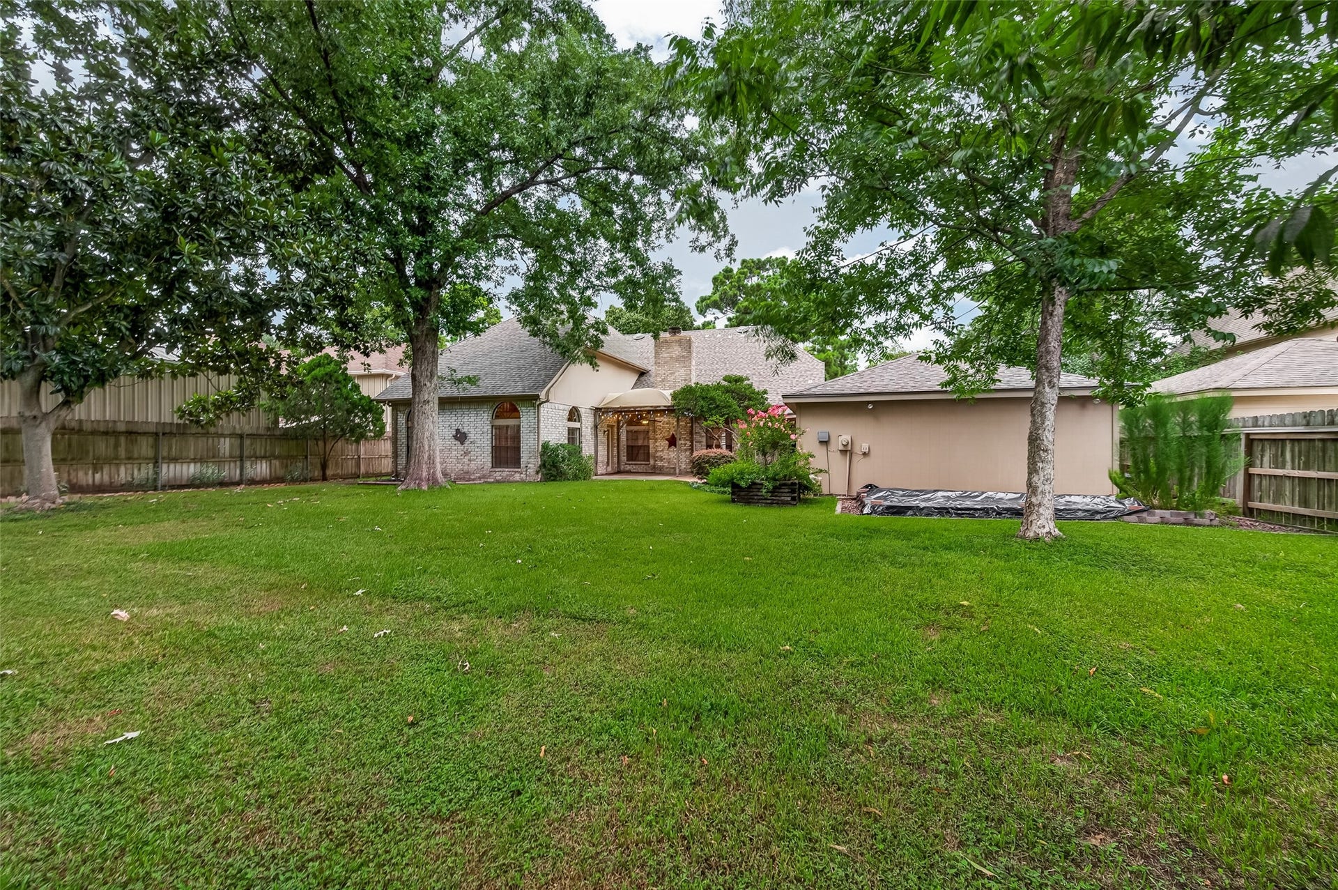 16405 Smith Street, Jersey Village, TX 77040 A rear view showcases the home's inviting outdoor spaces, from the covered pergola and expansive lawn to the mature shade trees that frame the backyard. Garden enthusiasts will appreciate the raised garden bed tucked behind the garage, complete with dedicated irrigation for customized watering of vegetables, herbs, flowers, or your favorite plants.