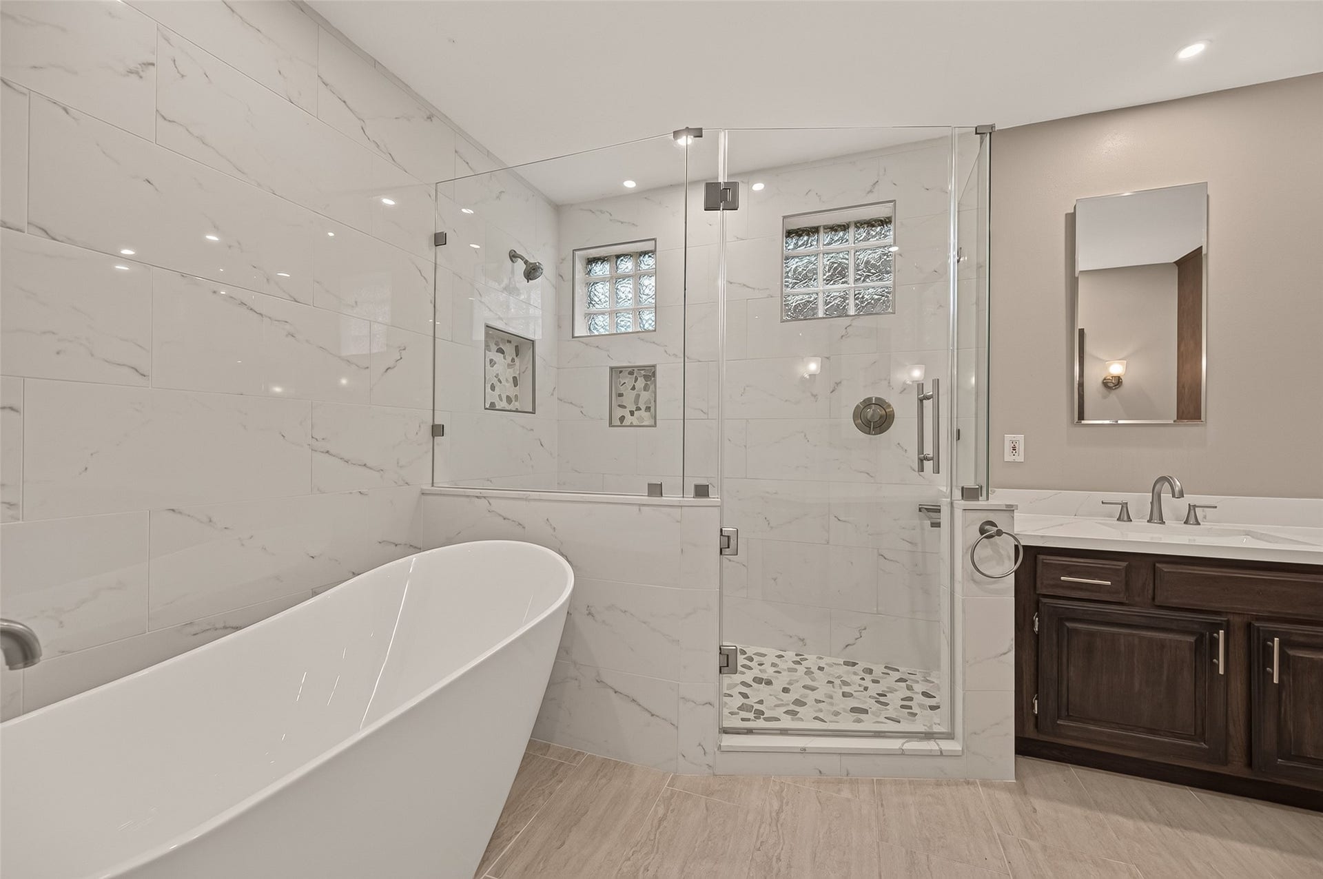 16405 Smith Street, Jersey Village, TX 77040 The true centerpiece of the 2021 remodel is this spa-inspired retreat. Unwind in the elegant freestanding soaking tub or step into the oversized walk-in shower featuring a frameless glass enclosure, floor-to-ceiling marble-look tile, pebble tile flooring, decorative accent niches, a built-in bench, and glass block windows that fill the space with natural light while maintaining privacy.
