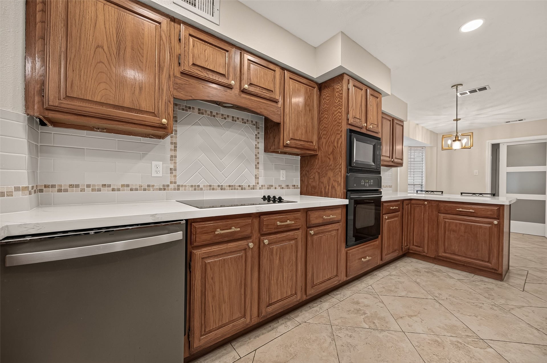 16405 Smith Street, Jersey Village, TX 77040 Whether preparing a quick weeknight dinner or your favorite family recipes, you'll appreciate the well-equipped cooking area featuring a Frigidaire 4-burner smooth glass cooktop, GE built-in microwave, GE wall oven, and GE dishwasher. Pull-out trays beneath the cooktop keep pots and pans neatly organized and within easy reach, while the decorative herringbone tile accent adds a timeless finishing touch.