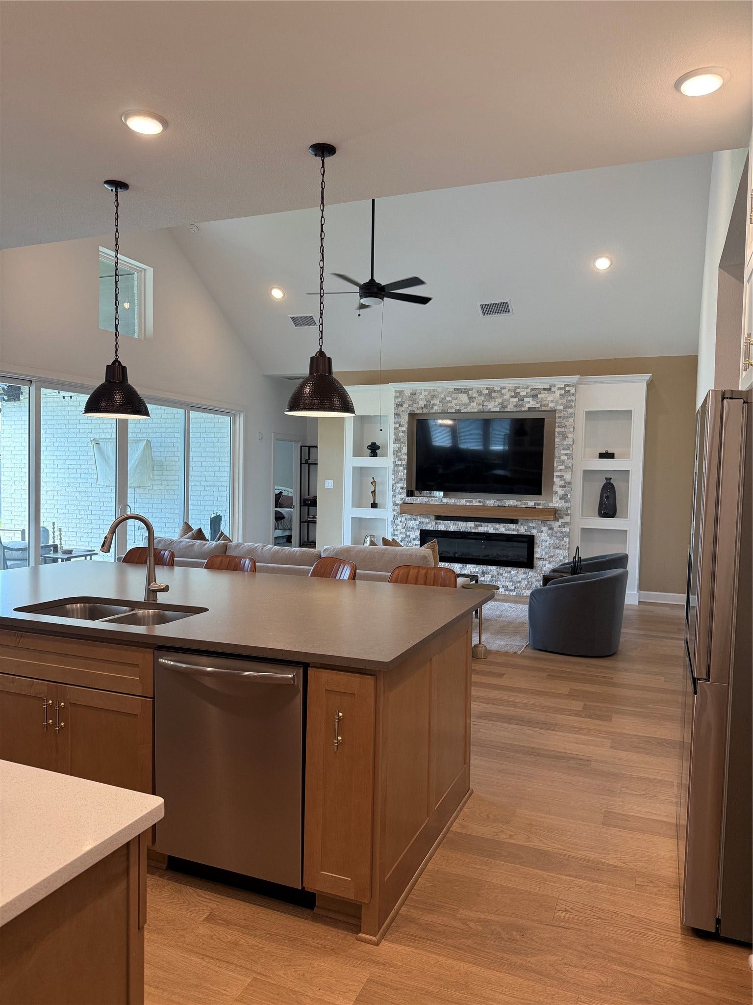 9911 Deep Water Drive, Missouri City, TX 77459 Spacious open-concept living area featuring a modern kitchen with a large island, sleek appliances, and stylish pendant lighting, seamlessly flowing into a cozy living room with a custom designed fireplace and built-in shelving.