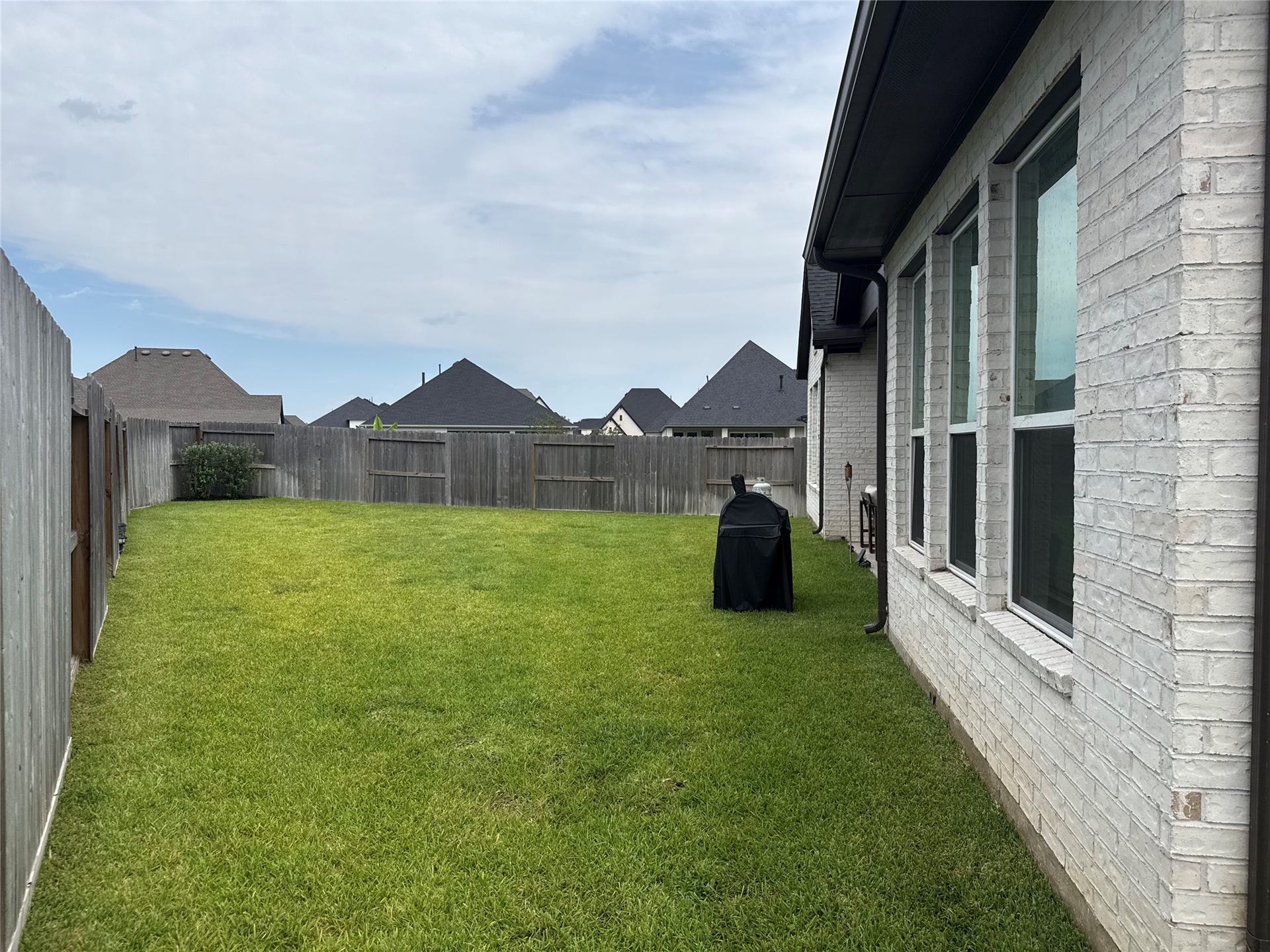 9911 Deep Water Drive, Missouri City, TX 77459 Spacious backyard with well-maintained lawn, privacy fencing, and a side view of the home's brick exterior featuring large windows, perfect for outdoor activities and relaxation.