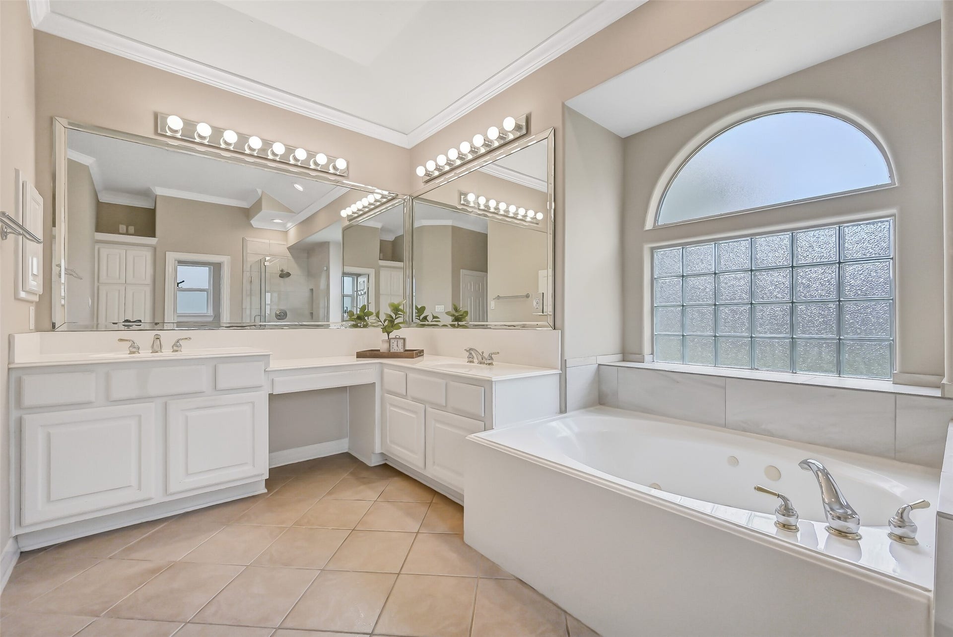 1813 Sandy Lake Drive, Friendswood, TX 77546 Another view highlights the generous separate vanities and dedicated seated makeup area, providing plenty of personal space and storage. The oversized jetted tub is framed by a distinctive glass-block window and arched transom for natural light with privacy.