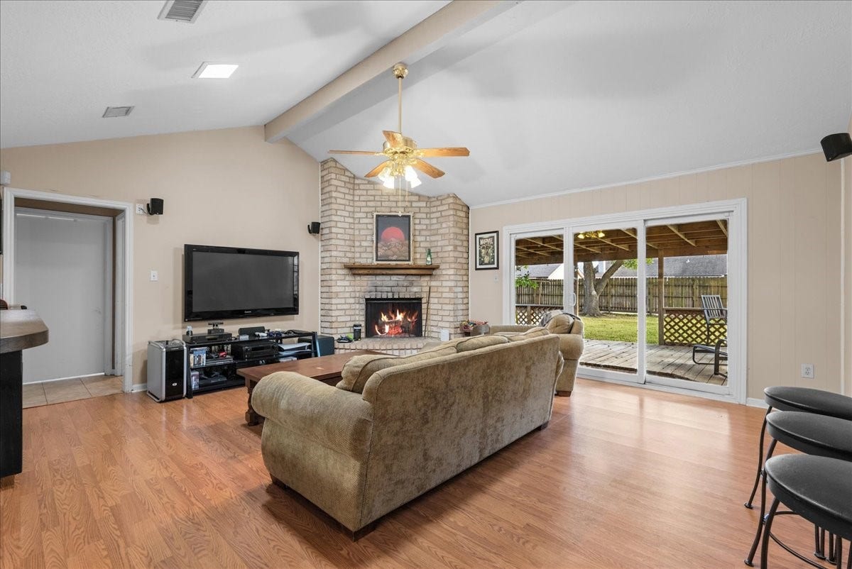 214 Oakwood Street, League City, TX 77573 Spacious living room with vaulted ceiling, brick fireplace, and sliding glass doors leading to the covered deck.