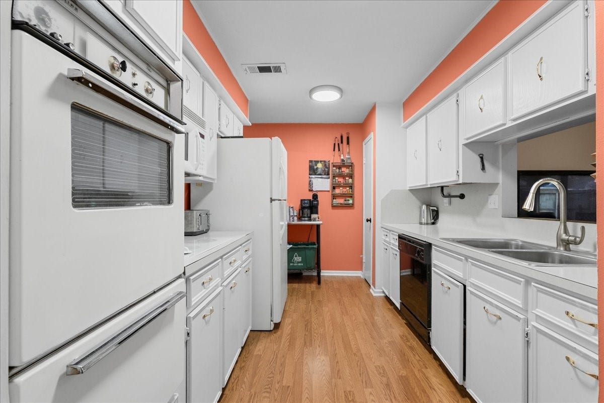 214 Oakwood Street, League City, TX 77573 Galley-style kitchen with abundant white cabinetry, built-in oven, and microwave.