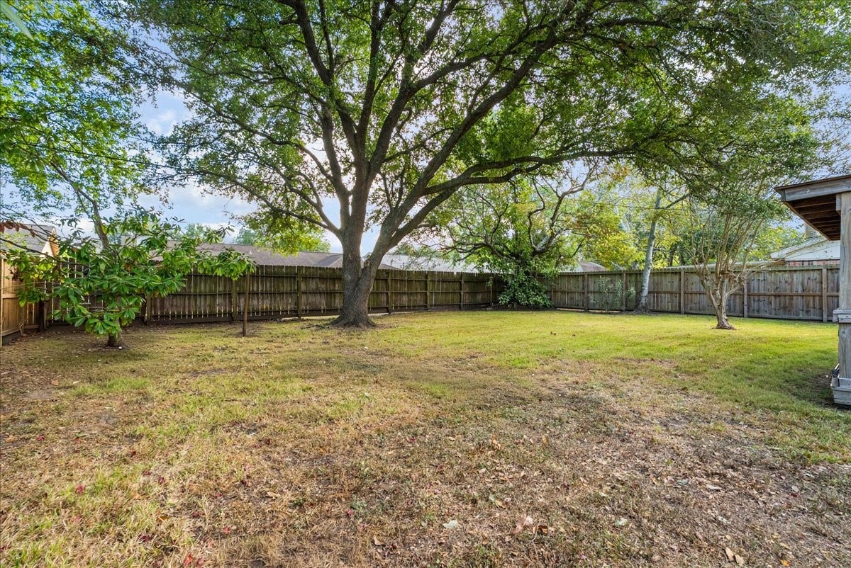 214 Oakwood Street, League City, TX 77573 Fenced backyard with mature shade trees and open lawn space for outdoor enjoyment.