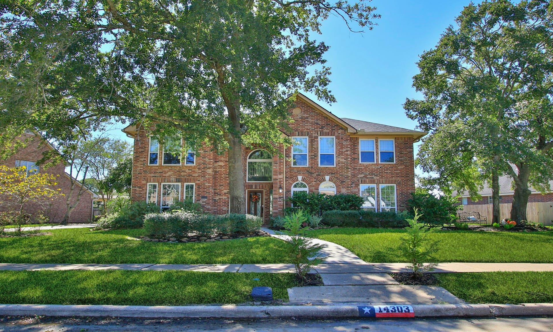 14303 Spyglen Lane, Cypress, TX 77429 Stately two-story brick home set amidst lush greenery and mature trees, featuring a charming pathway leading to an elegant arched entryway.
