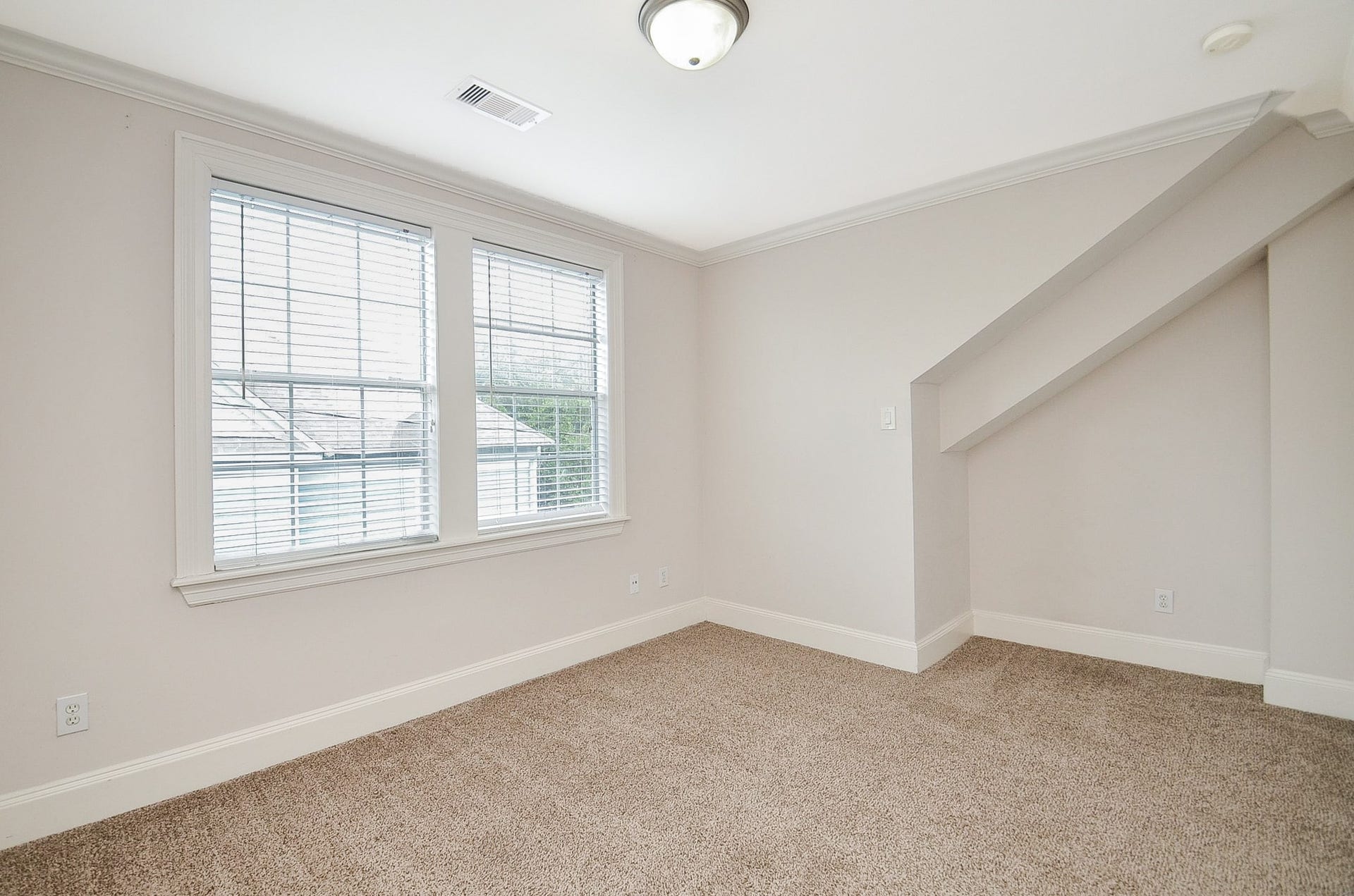 Bright and cozy primary bedroom with a large window, plush carpeting, and a charming nook.