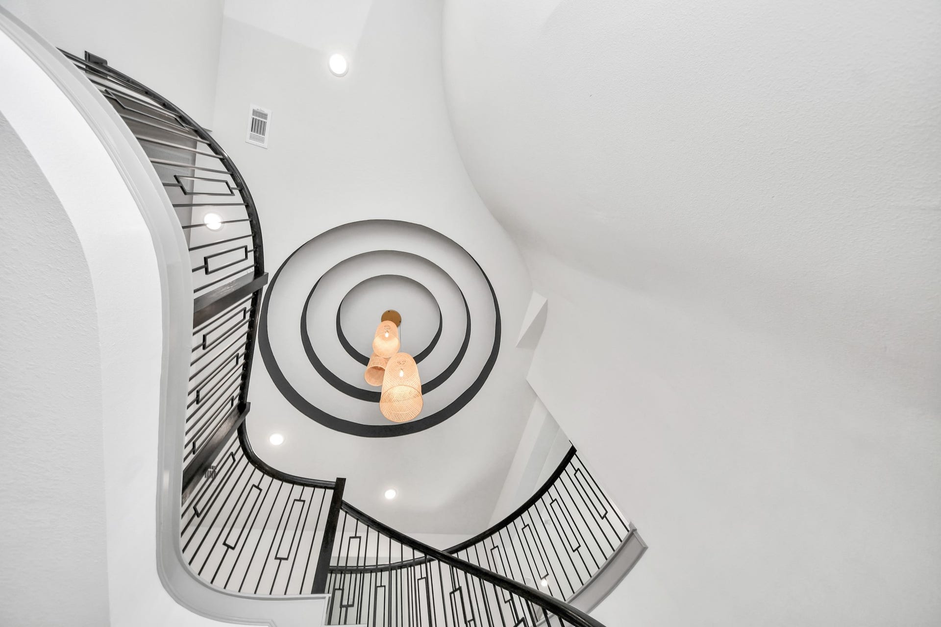 1423 Hackberry Heights Drive, Richmond, TX 77406 A striking spiral staircase with elegant wrought iron railings leads upward, highlighted by a modern, cascading chandelier and a dramatic circular ceiling design.