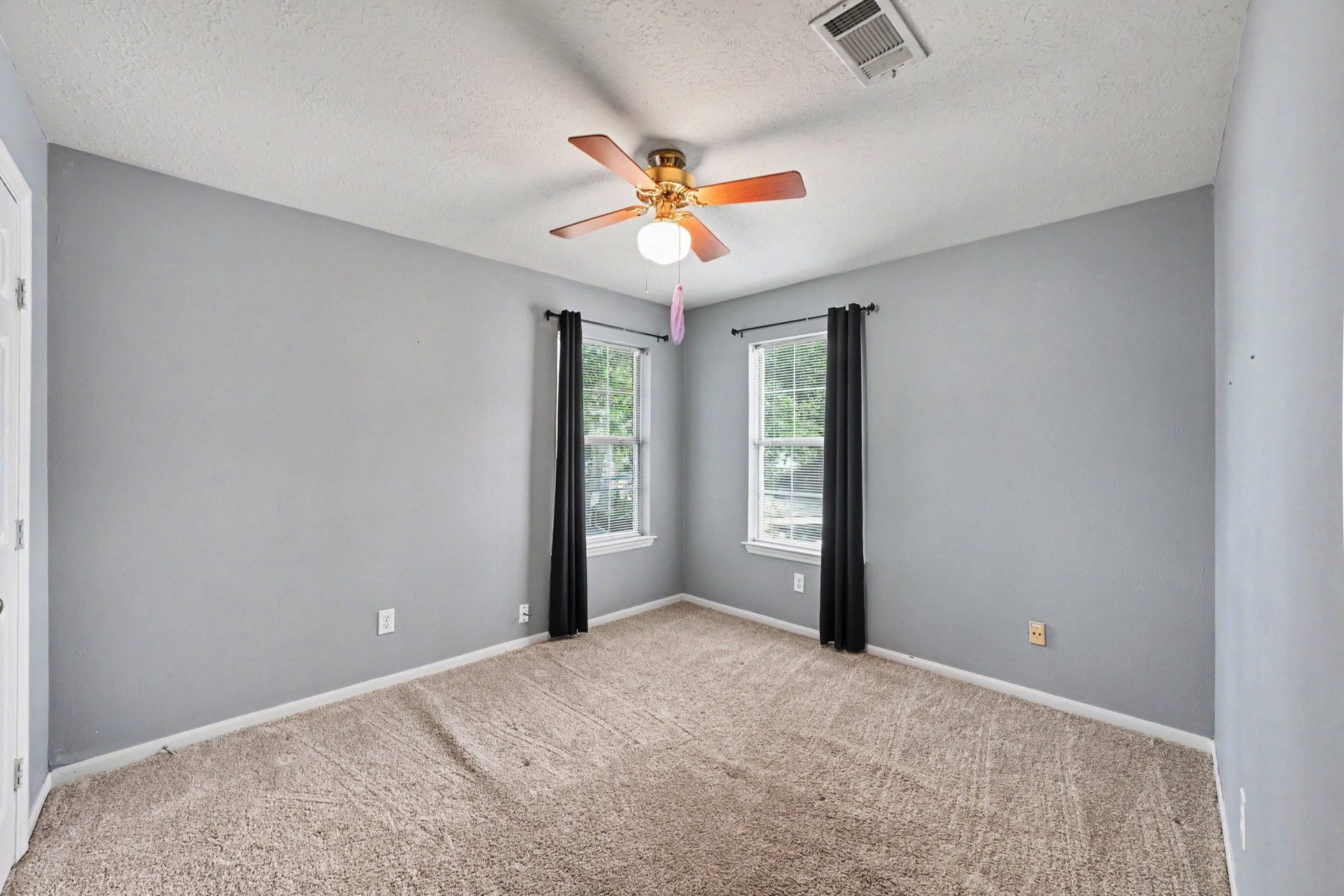 17510 Tall Maple Court, Houston, TX 77095 This upstairs secondary bedroom features soft gray walls, plush carpeting, and two windows that bring in plenty of natural light. A ceiling fan and comfortable layout make this an inviting space for family or guests.