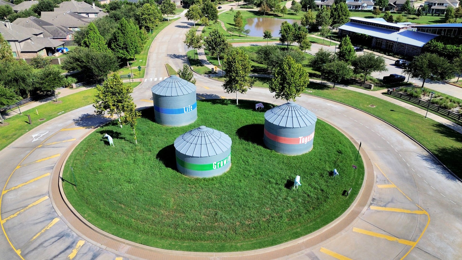 1423 Hackberry Heights Drive, Richmond, TX 77406 Located in a picturesque neighborhood, this charming roundabout features unique cylindrical structures surrounded by lush greenery and mature trees, offering a serene and inviting community atmosphere.