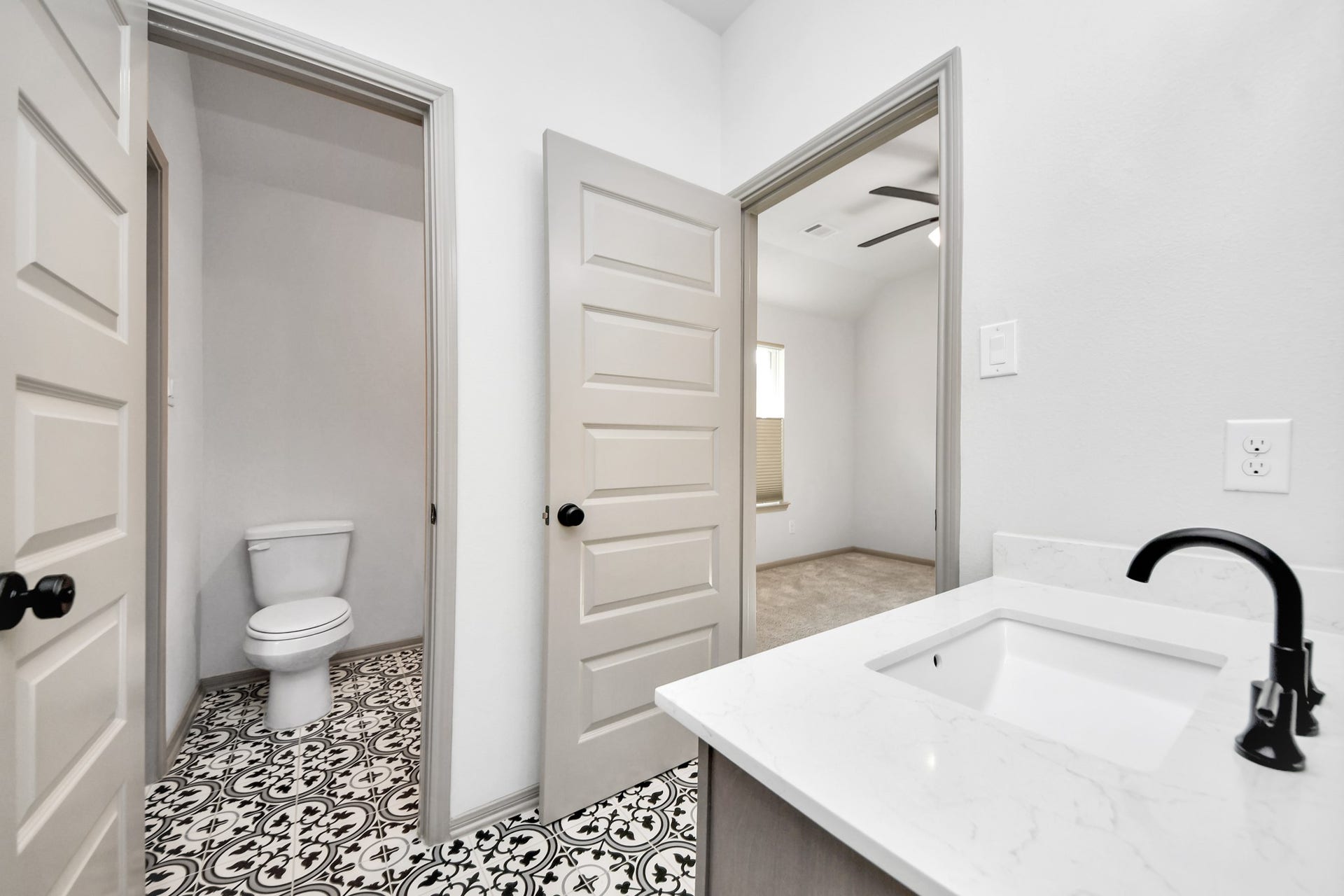 1423 Hackberry Heights Drive, Richmond, TX 77406 Modern bathroom features a sleek vanity with a black faucet and eye-catching patterned floor tiles leading to a private toilet area.