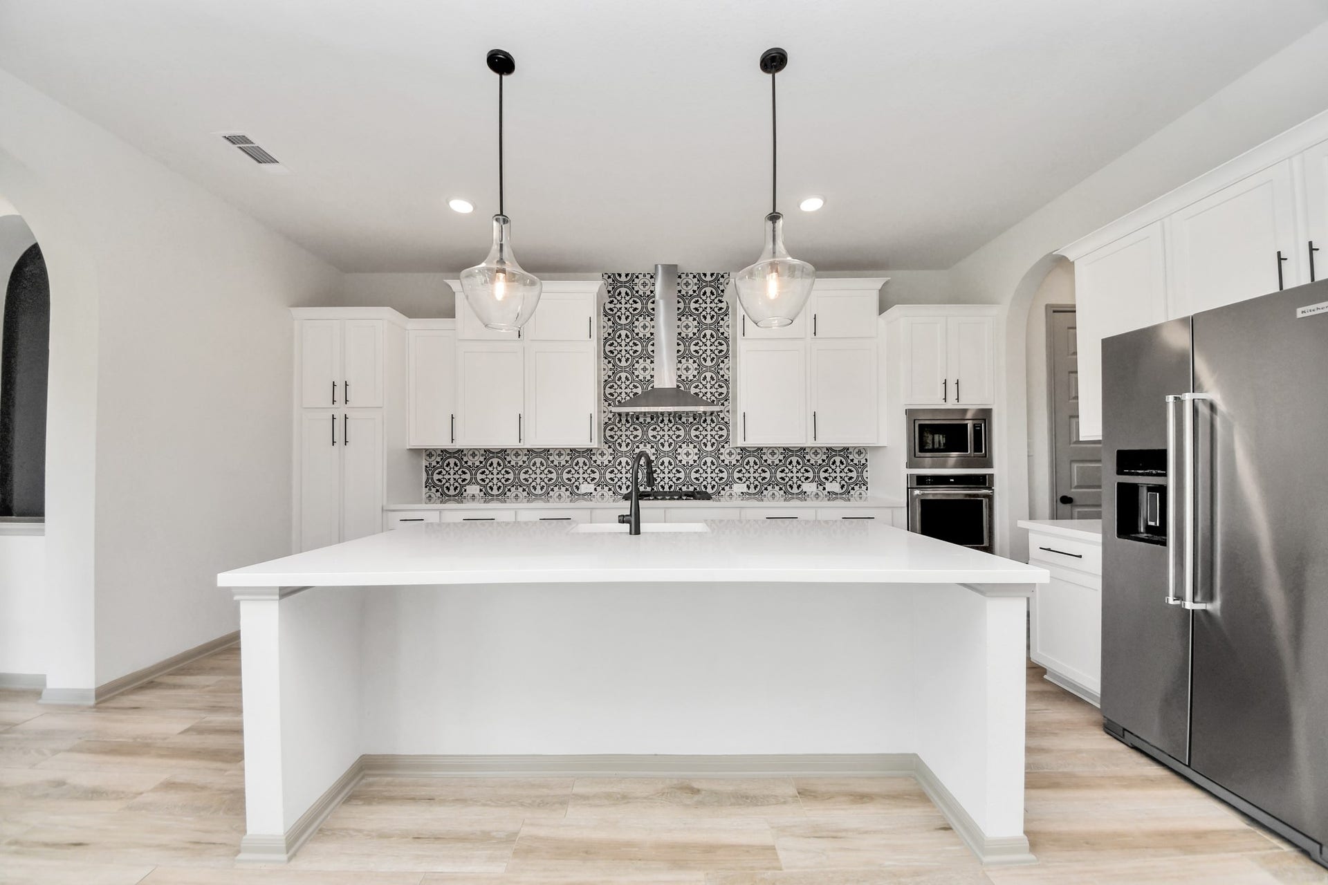 1423 Hackberry Heights Drive, Richmond, TX 77406 Stunning modern kitchen with a spacious island, elegant pendant lighting, and stylish black and white tile backsplash, complemented by sleek stainless steel appliances.