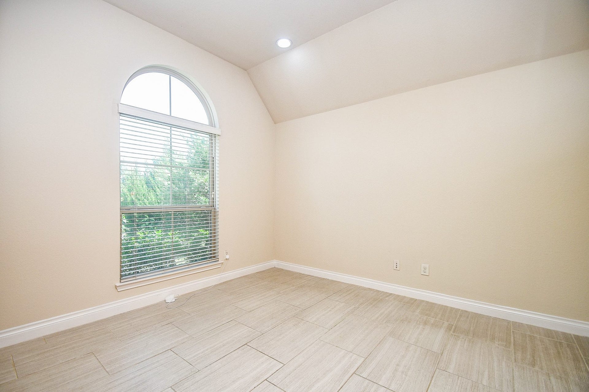 A bright, inviting  study room with neutral walls, a stunning arched window flooding natural light onto the light- tile flooringperfect for a home office or guest retreat.