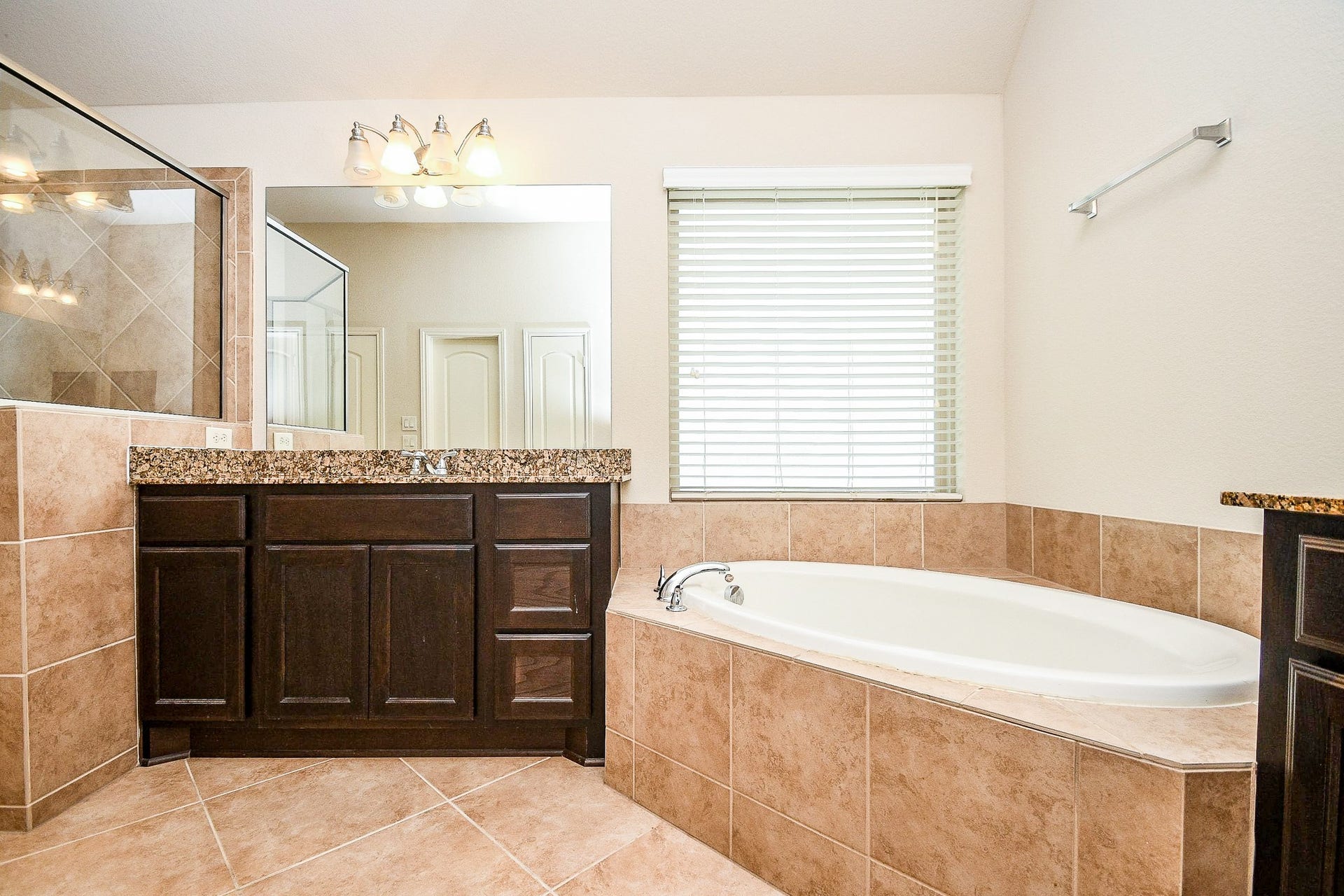 Indulge in relaxation with a spacious soaking tub, elegant granite countertop, and dark wood vanity, all complemented by warm tile accents and abundant natural light from a generous window.