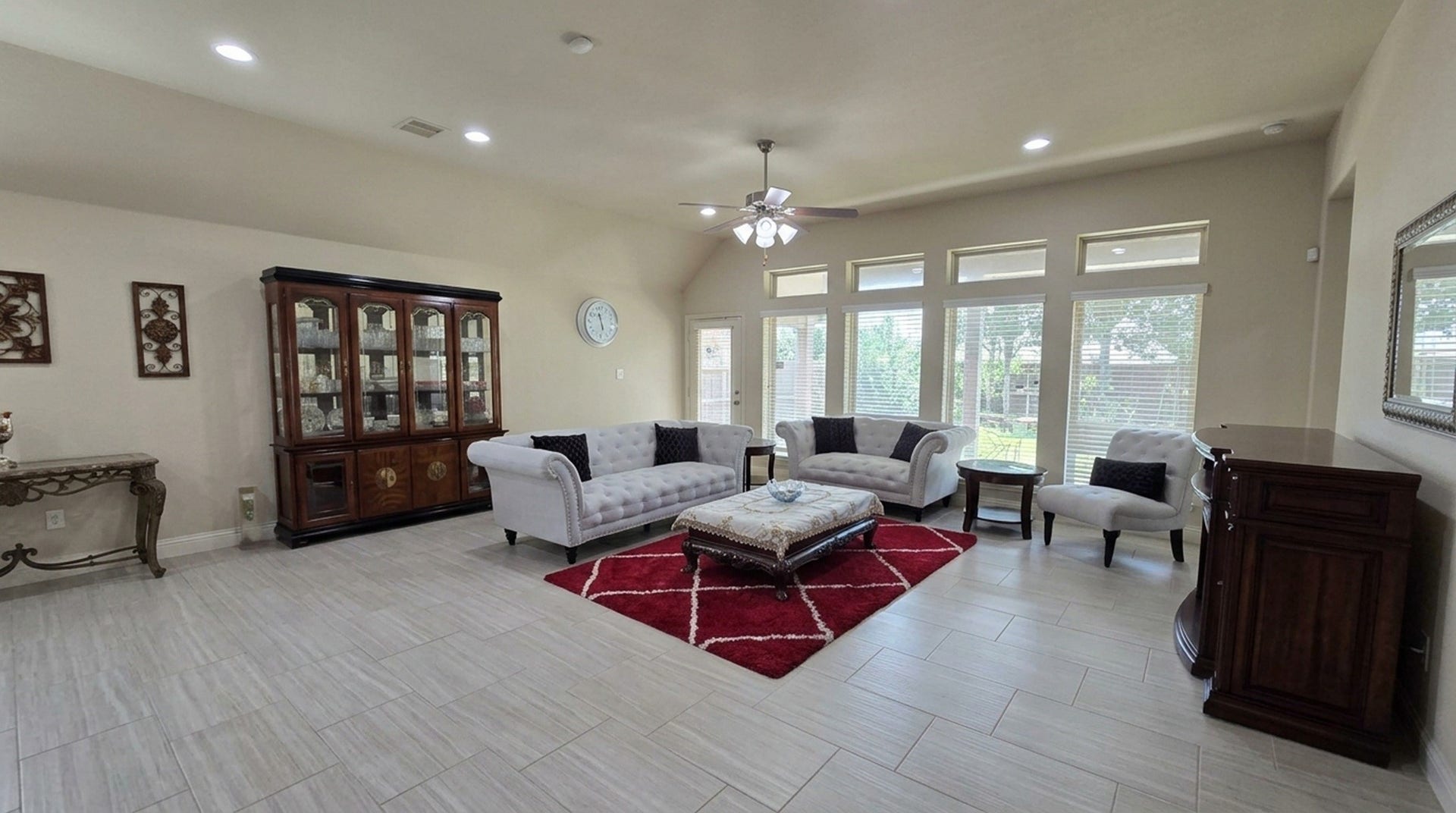 Spacious and elegant living room featuring large windows, abundant natural light, stylish furnishings, and a striking red area rug, perfect for relaxation and entertaining.