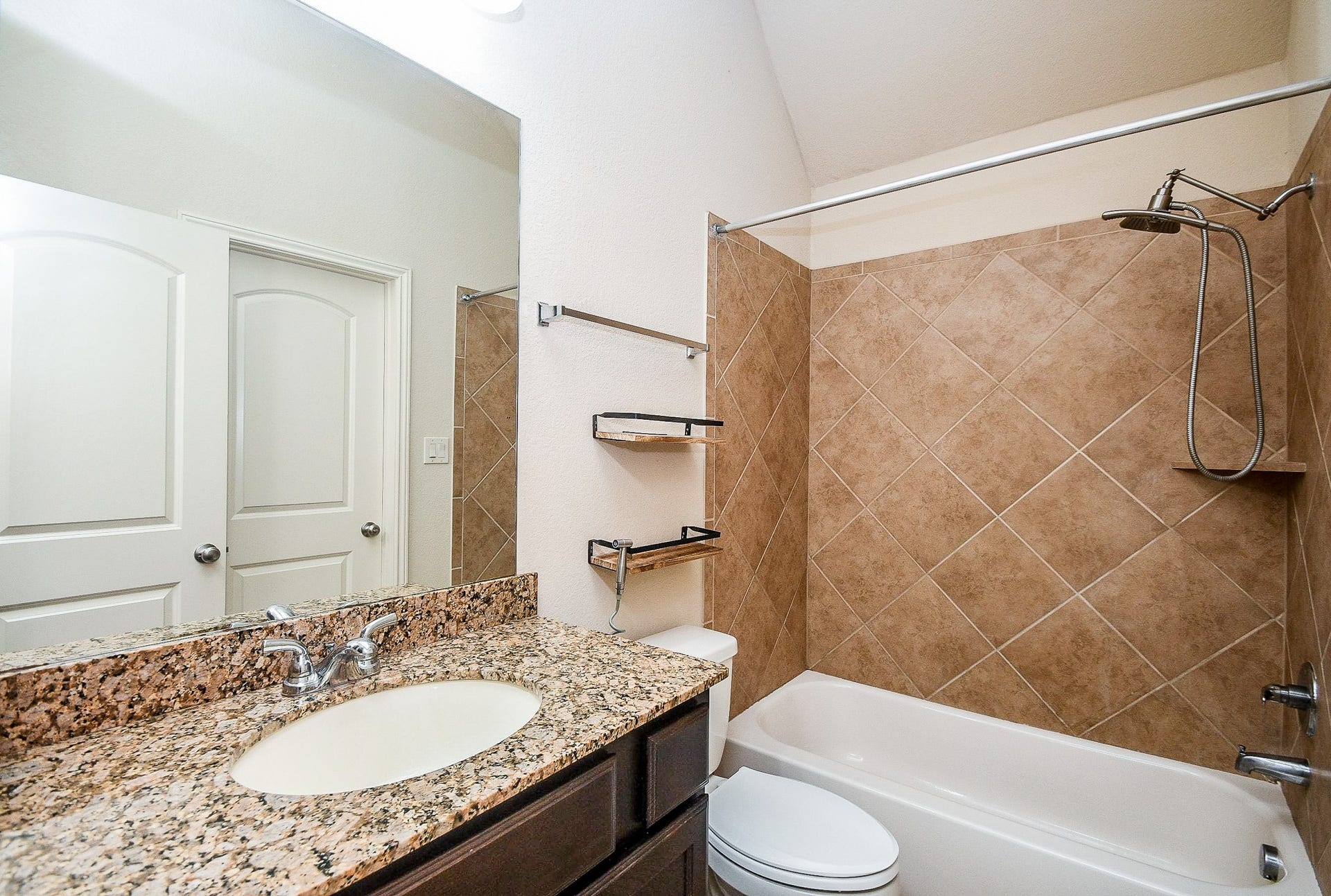This bathroom features a granite countertop with a modern sink, a tile backsplash, and a bathtub with a tiled shower area. It has a clean, neutral design with ample lighting and storage shelves.