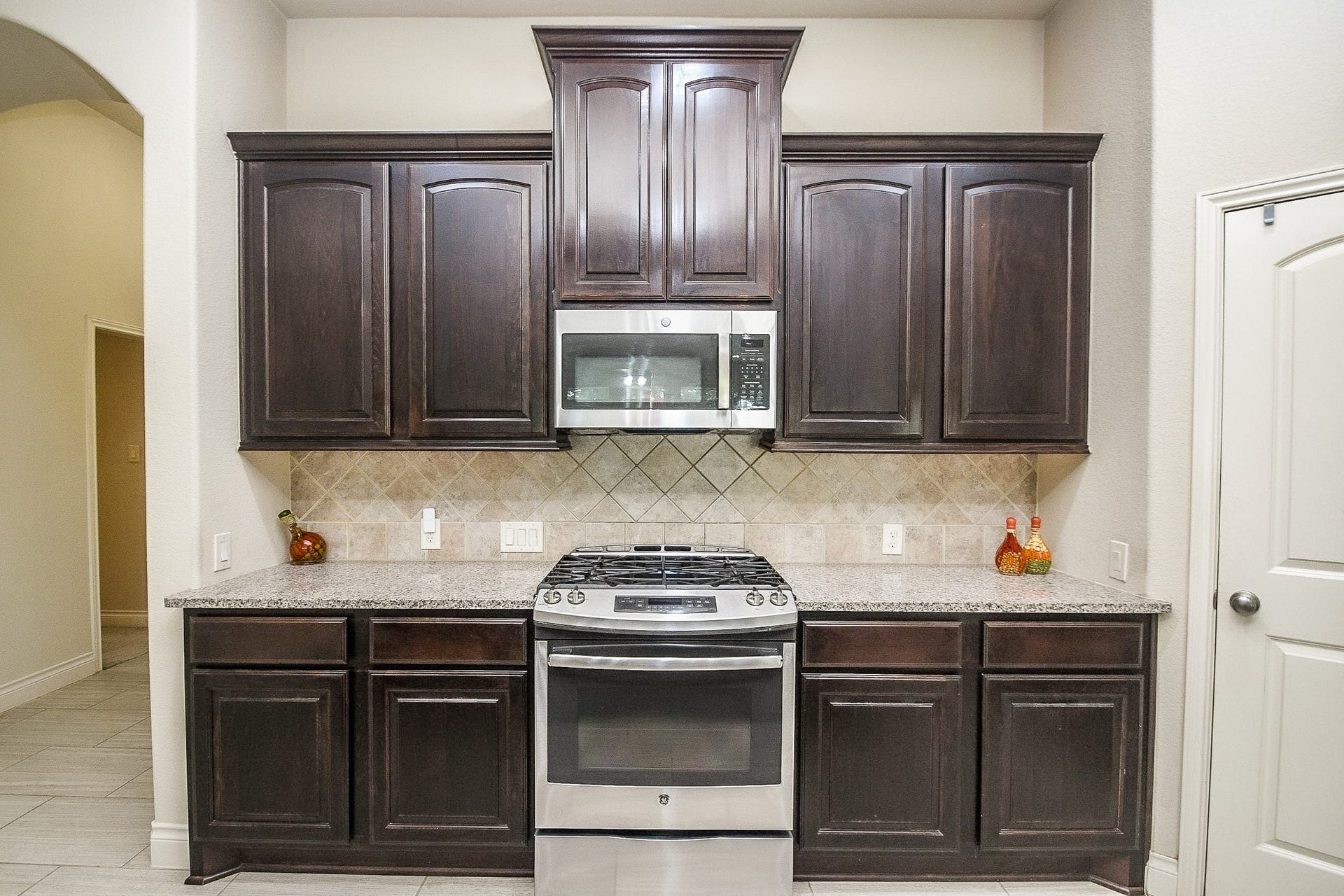 Discover a modern and functional kitchen with rich dark wood cabinets, elegant granite countertops, a built-in microwave, and a sleek stainless steel gas stove.