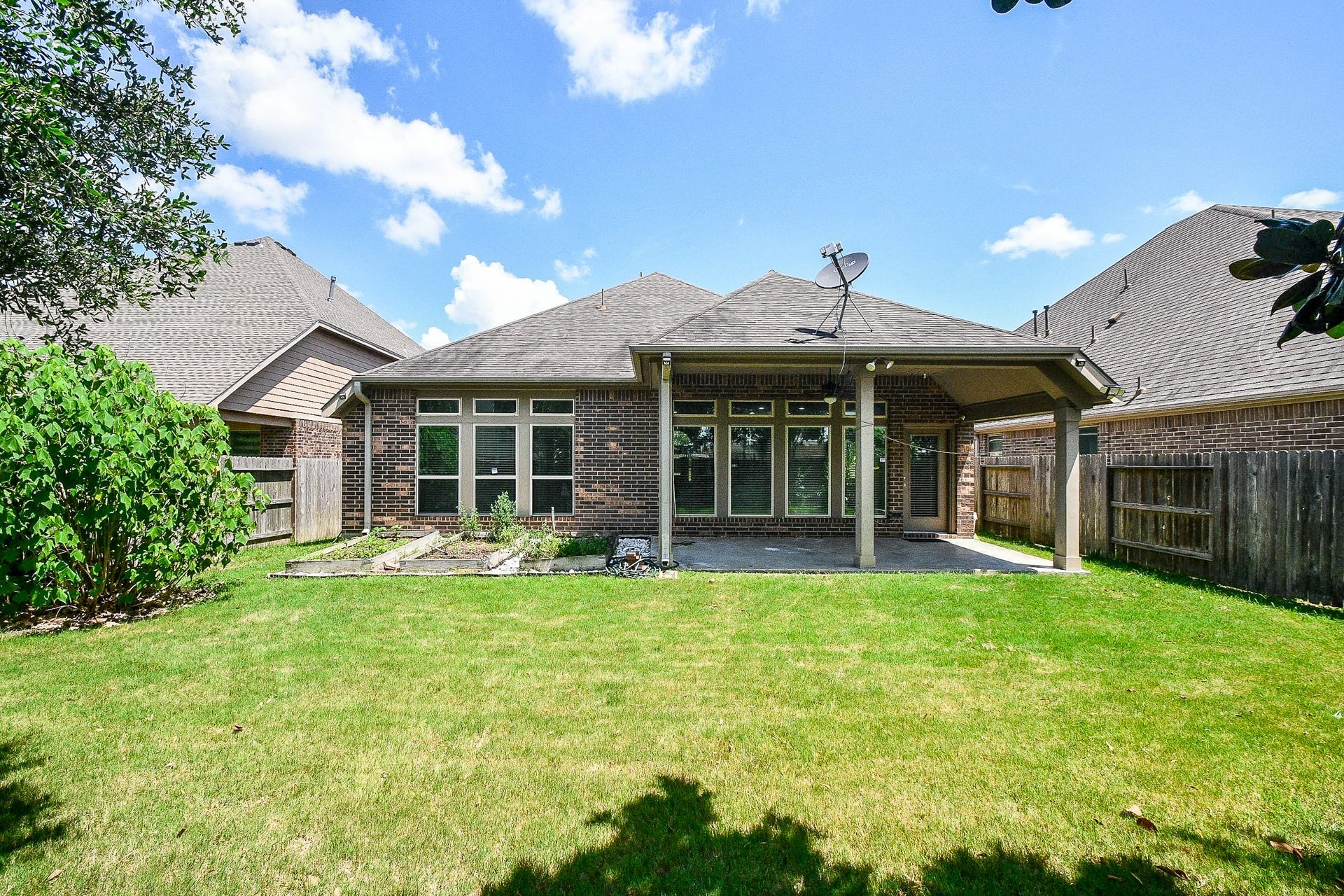This photo shows a well-maintained backyard with a covered patio, brick exterior, and a neatly landscaped garden. The fenced yard offers privacy and ample space for outdoor activities.