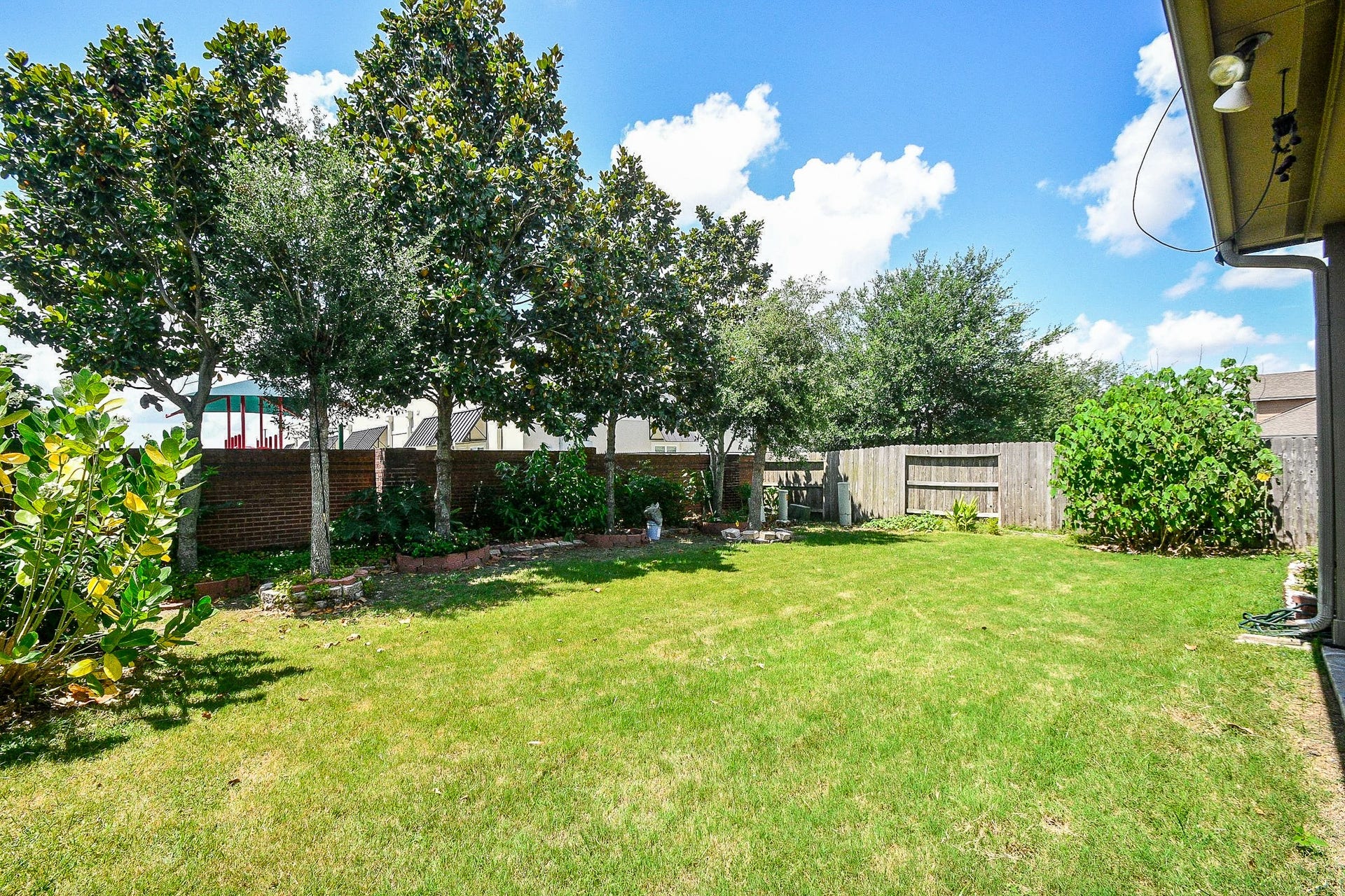 Spacious backyard with lush green lawn, mature trees, and a wooden fence for privacy. Ideal for outdoor activities and relaxation.