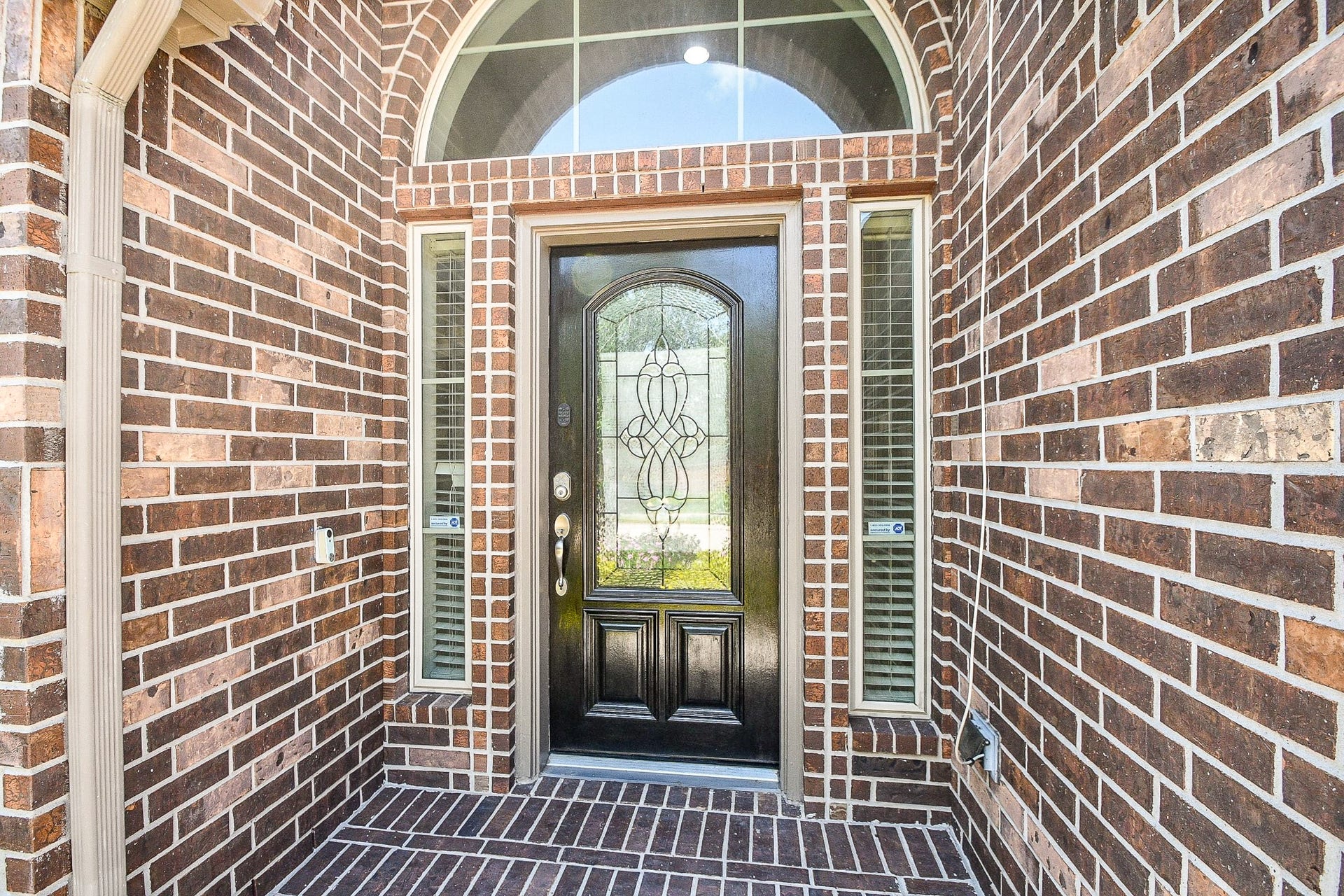 A striking dark front door with decorative glass panels, flanked by narrow windows, complements the charming brick exterior, enhancing this home's inviting curb appeal.
