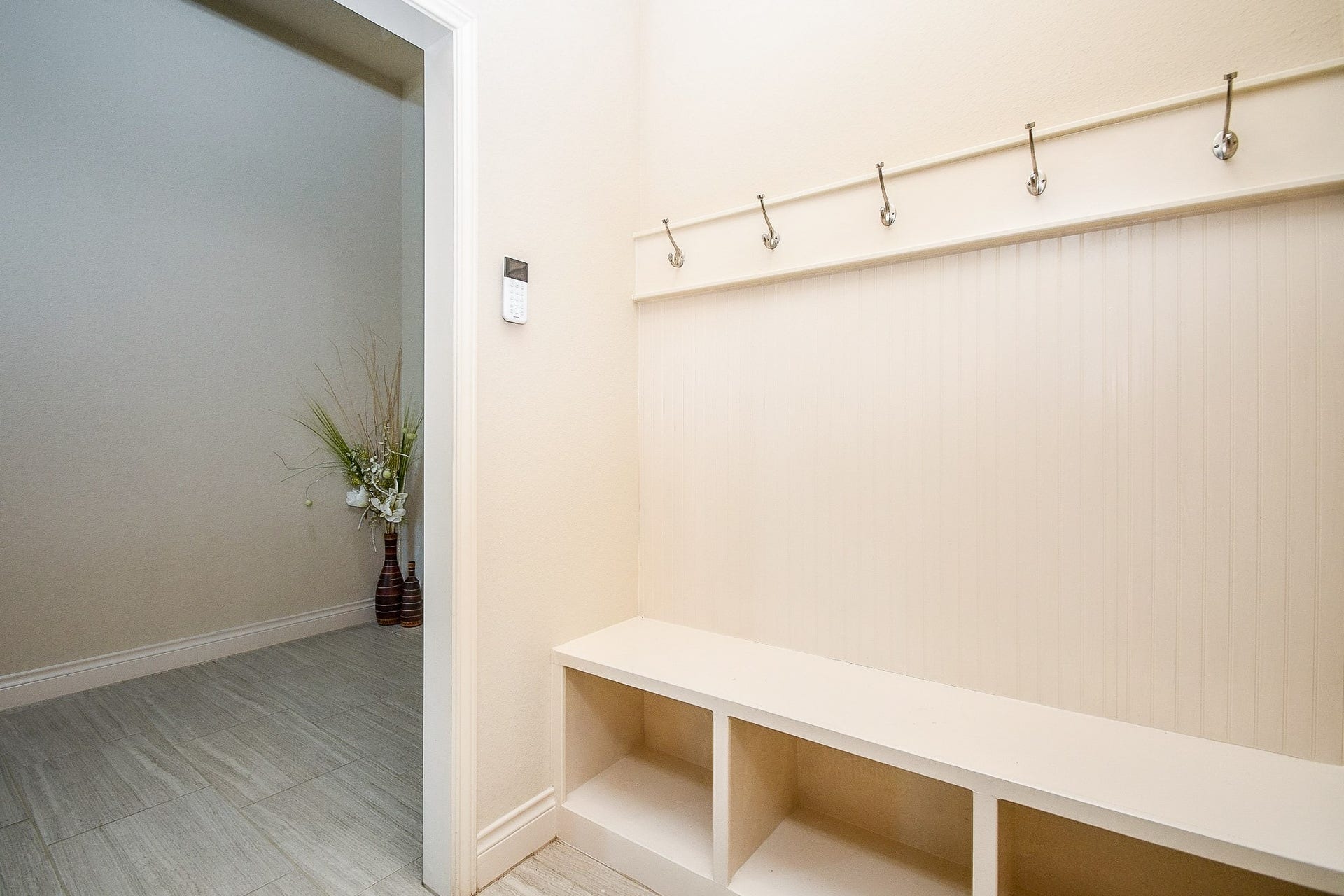 Bright and inviting, this entryway features a built-in bench with storage cubbies and coat hooks for ultimate organization, complemented by light walls and flooring, with a decorative vase adding a touch of elegance.