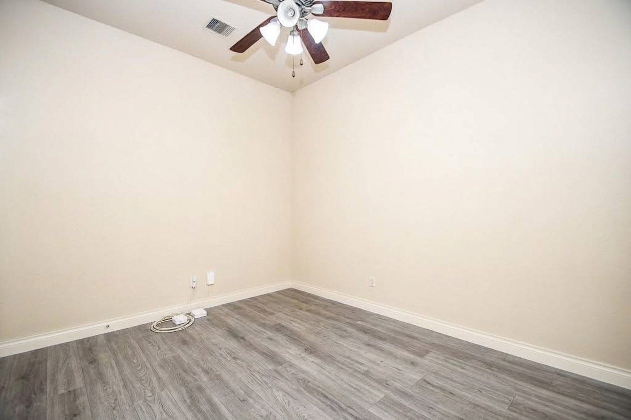 Bright and versatile room featuring sleek wood-look flooring and a ceiling fan, perfect for customization to suit your needs.