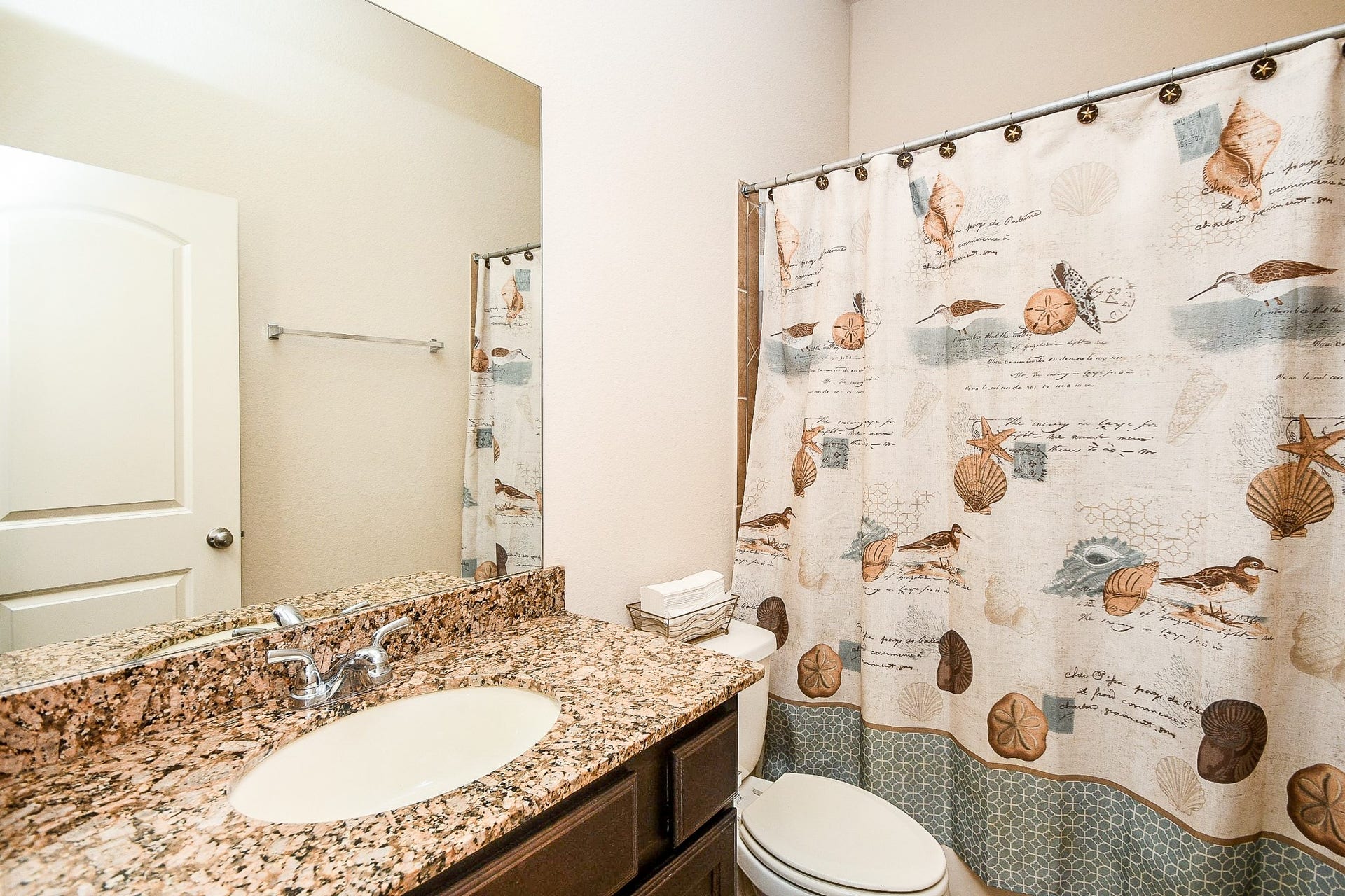 Bright and inviting, this bathroom boasts a granite countertop, large mirror, and a stylish shower with a decorative curtain, complemented by light walls and door for a clean, refreshing atmosphere.