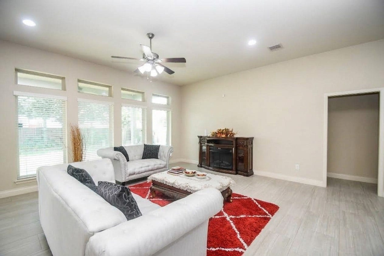 Bright and spacious living room featuring large windows, elegant seating, and a cozy fireplace, all accented by a stylish red area rug.
