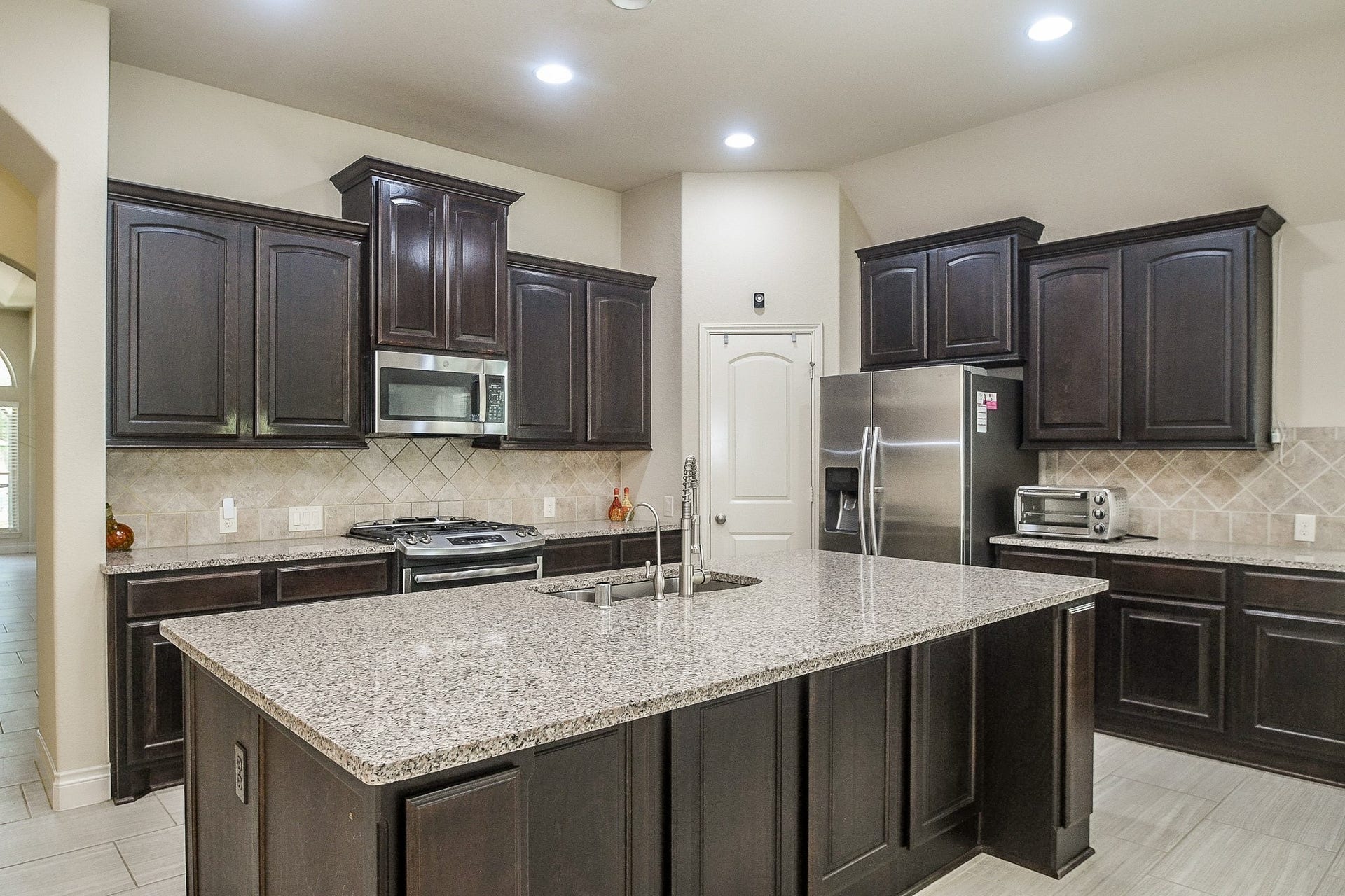 A culinary enthusiast's dream, this spacious kitchen boasts elegant dark wood cabinets, sleek granite countertops, and modern stainless steel appliances, with a large central island perfect for cooking and entertaining.