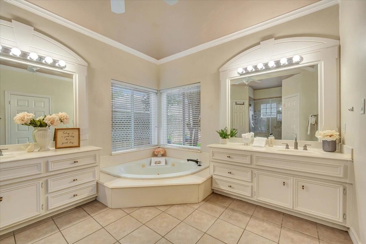 Primary bath features dual vanities, a corner jacuzzi oaking tub and abundant natural light.
