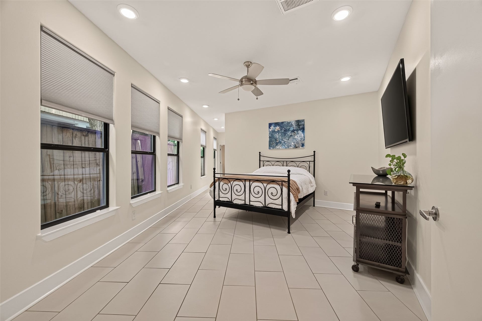 This spacious first floor bedroom features large windows with blinds, a ceiling fan, and recessed lighting.