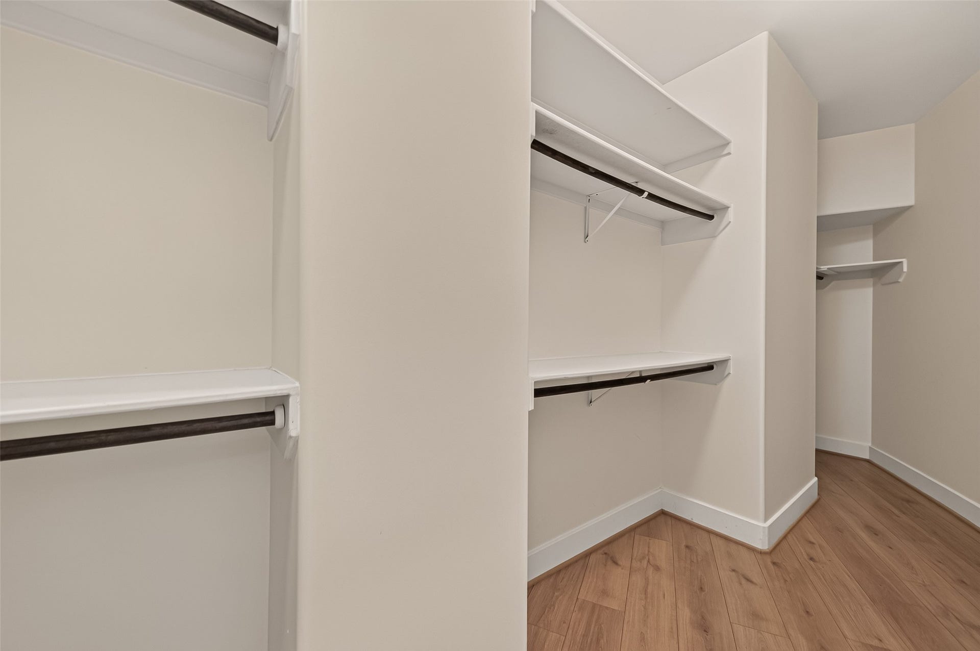 Spacious walk-in closet with multiple shelves and hanging rods, with neutral walls for a clean, organized look.