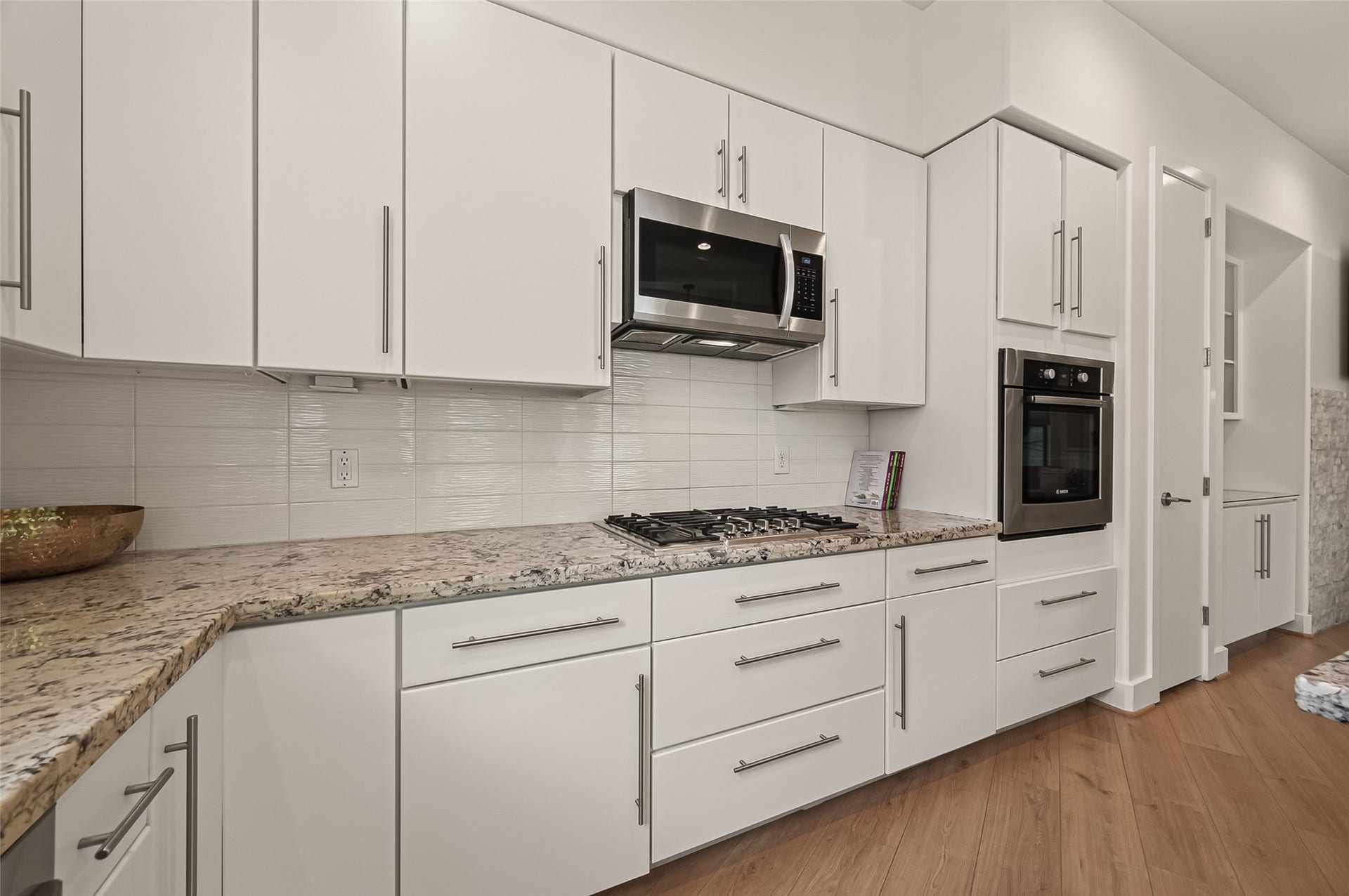 Modern kitchen featuring sleek white cabinetry, granite countertops, stainless steel appliances, and a built-in wall oven. The space is bright and spacious with clean lines and a contemporary design.