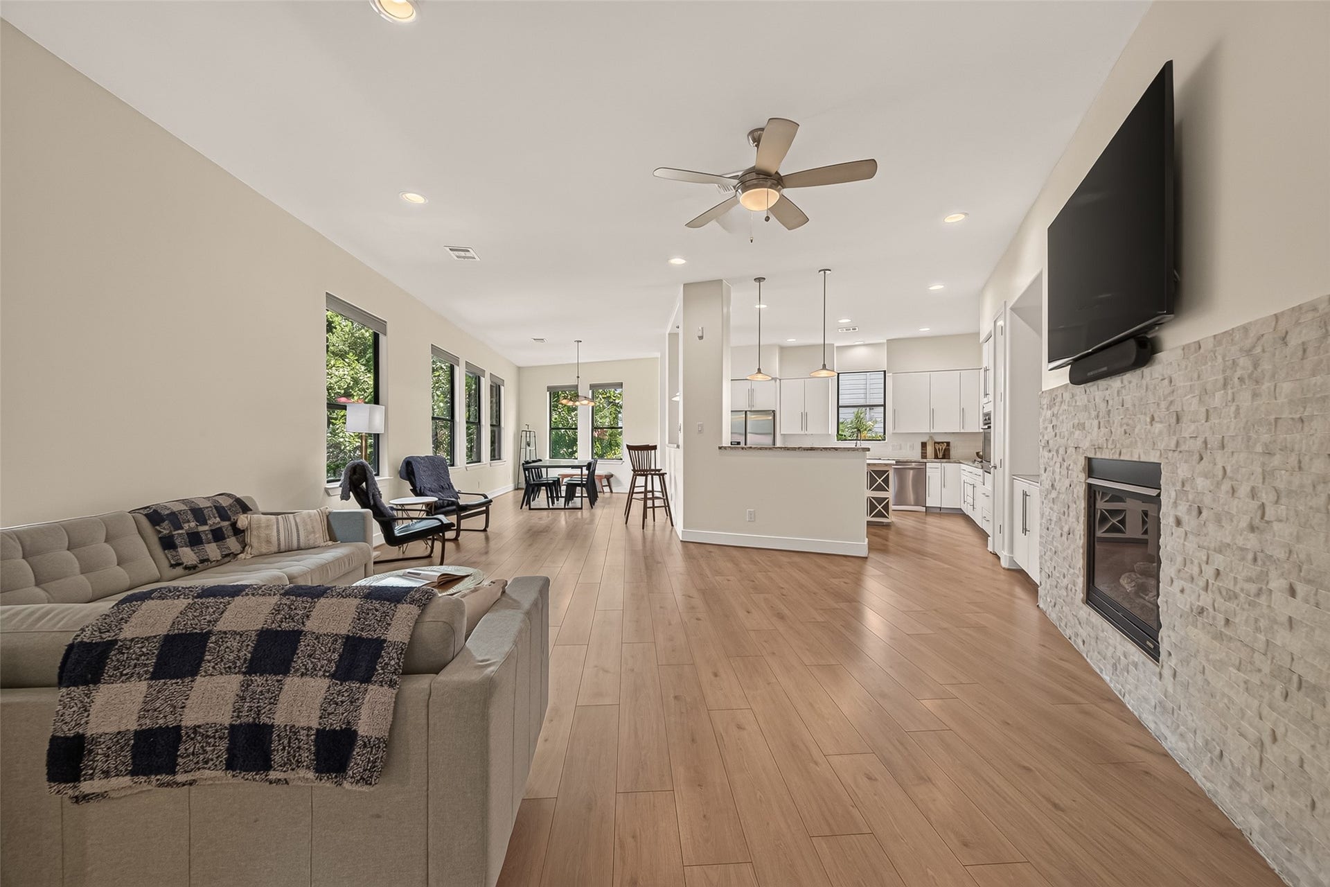 This open-concept living area features a modern kitchen with pendant lighting. The space is brightened by large windows and flooring, creating a welcoming and airy atmosphere.