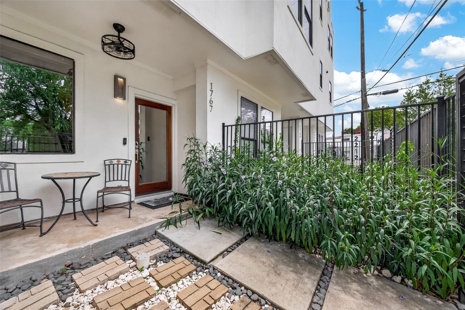 Charming front patio with lush greenery along a gated pathway. Perfect for relaxing and enjoying the outdoors.