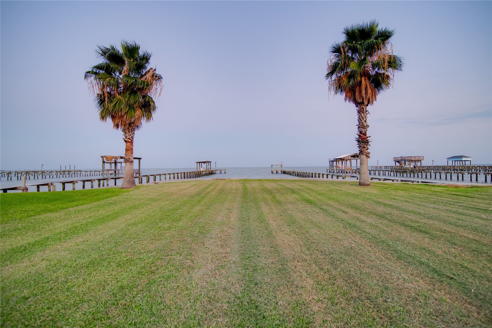 1309 8th Street, San Leon, TX 77539 How about transforming this large grassy space between the deck and the ocean into a versatile outdoor haven. Possibilities include creating a private garden with tropical or coastal plants, adding a fire pit area for evening gatherings, setting up a play area for children or pets, or installing an outdoor dining and lounge space to enjoy meals with panoramic water views. The open lawn also provides ample room for a pool, putting green, or other recreational features to enhance waterfront living.