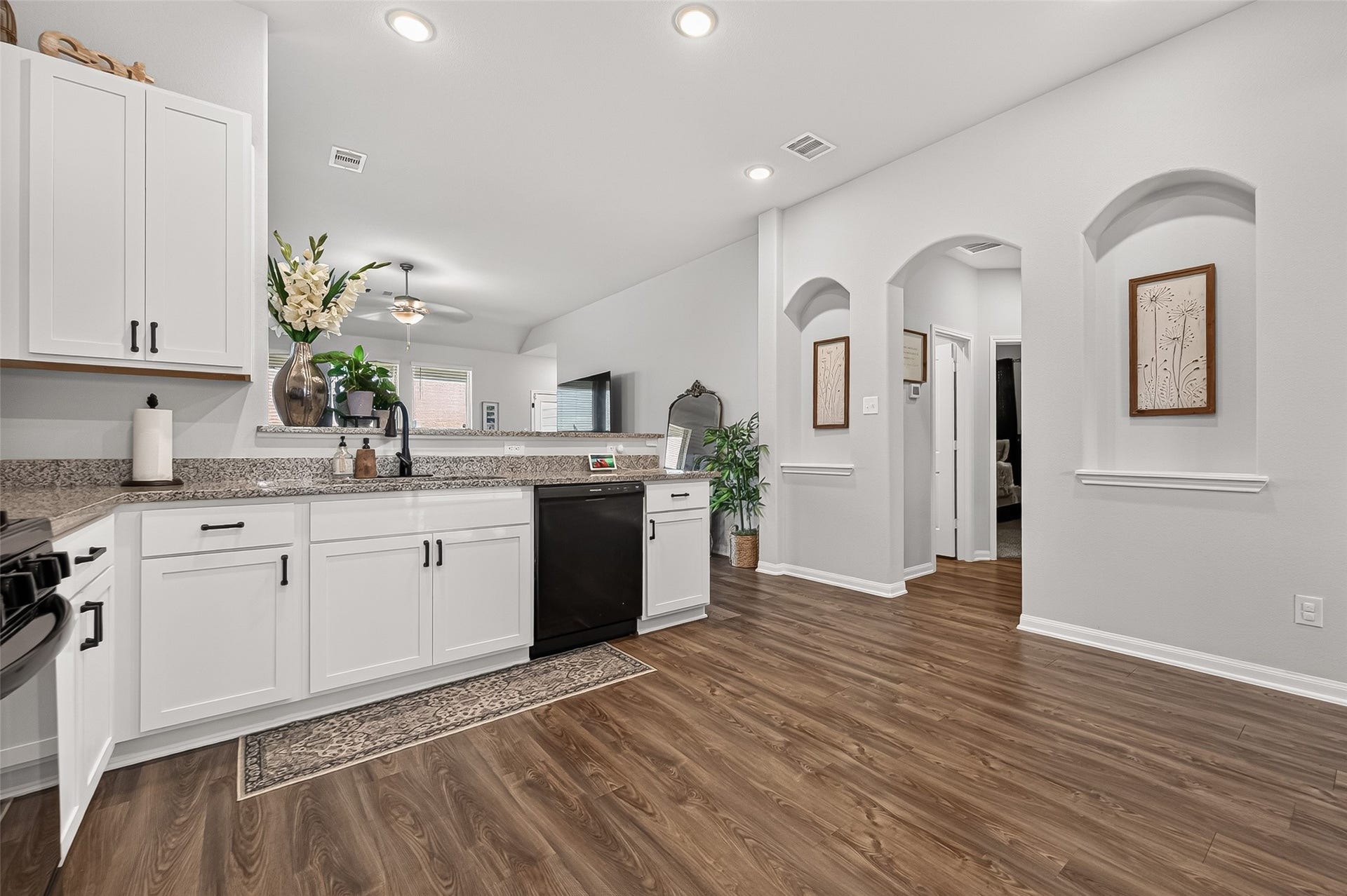 8422 Black Pearl Court, Texas City, TX 77591 Spacious kitchen with elegant white cabinetry, granite countertops, and modern black appliances, complemented by warm wood flooring and stylish archways.