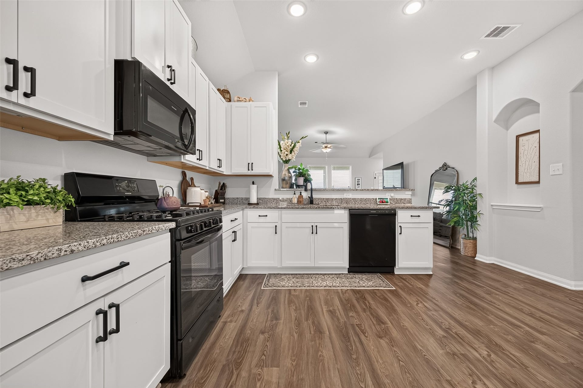 8422 Black Pearl Court, Texas City, TX 77591 A spacious kitchen with modern appliances, sleek granite countertops, and elegant white cabinetry, seamlessly connecting to a cozy living area with warm wood flooring.