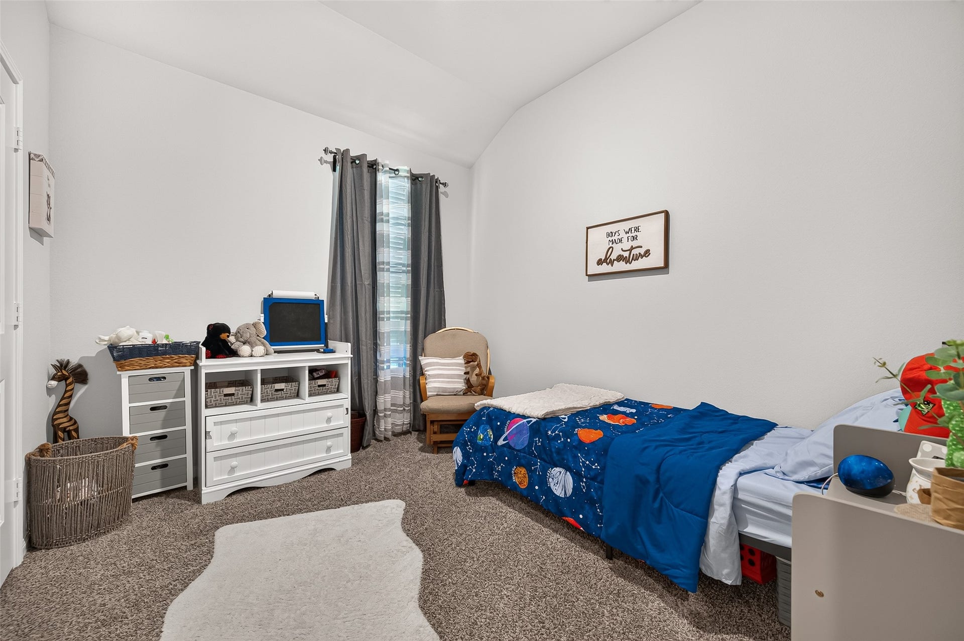 8422 Black Pearl Court, Texas City, TX 77591 Cozy children's bedroom featuring plush carpeting, a cheerful space-themed bedspread, and ample storage with a white dresser and shelves. Natural light streams in through the window, creating a bright and inviting atmosphere.