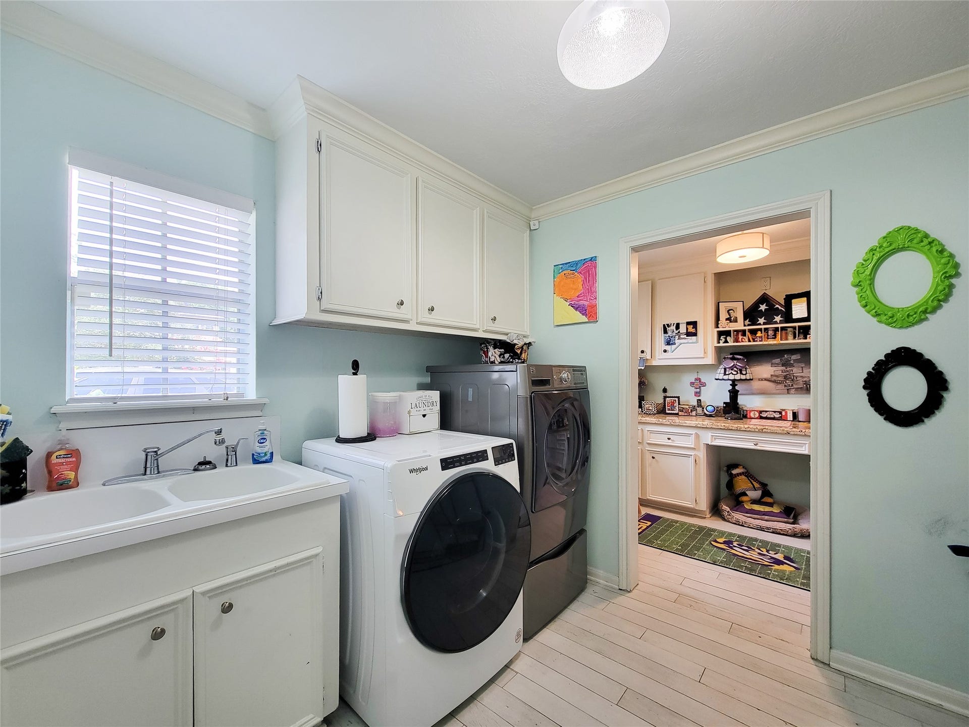6235 Rolling Water Drive, Houston, TX 77069 This photo shows a bright, functional laundry room with modern appliances, ample cabinet storage, and a sink. The adjacent area appears to be a cozy workspace or pet area, enhancing utility and convenience.