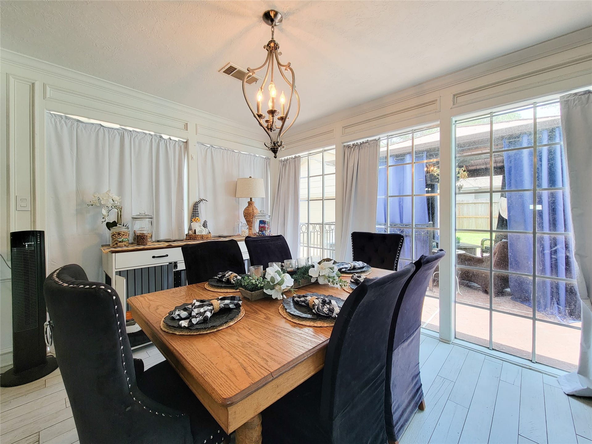 6235 Rolling Water Drive, Houston, TX 77069 Bright dining area with large windows, elegant chandelier, and a wooden table set for six. The space features light wood flooring and leads to an outdoor patio area, creating an inviting atmosphere for gatherings.